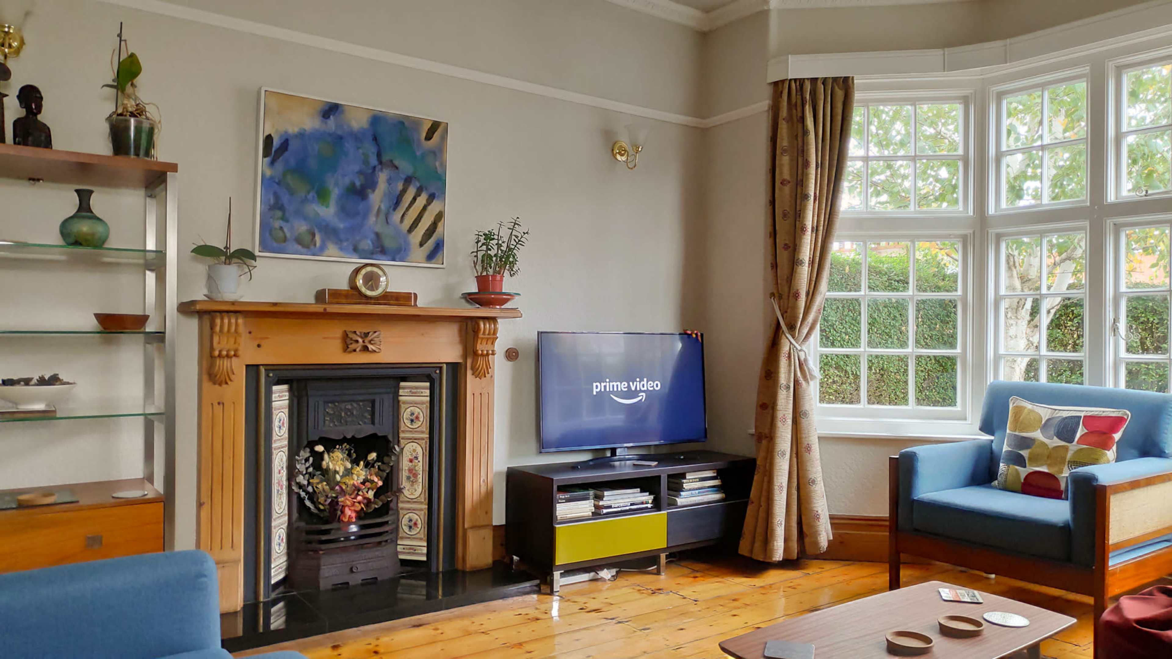 A living room with a television displaying the Prime Video logo, a fireplace with decorative elements, and windows providing natural light.