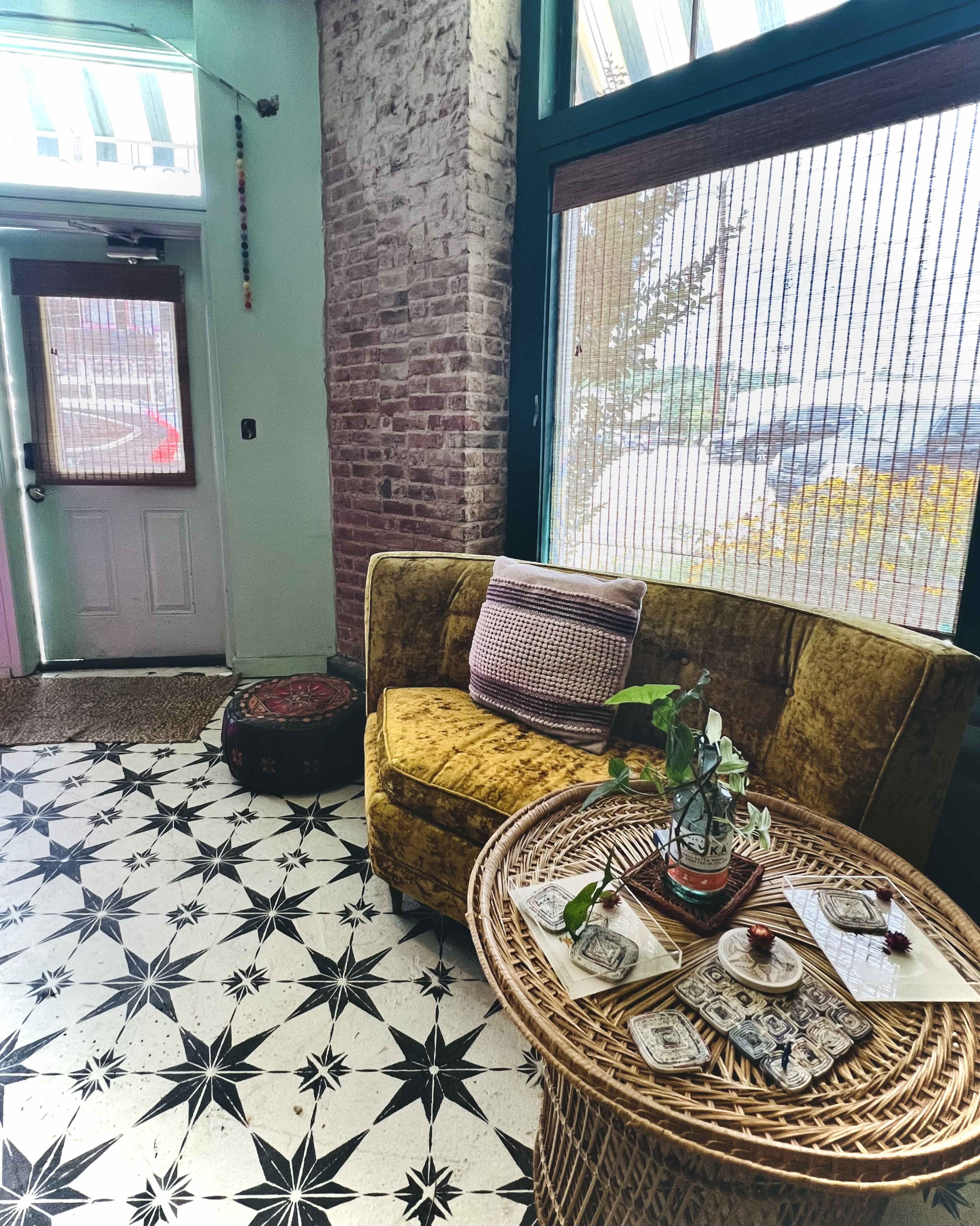 A cozy corner in a room with a yellow couch, a round wicker table adorned with decorative items, and a patterned floor that features black and white star shapes.