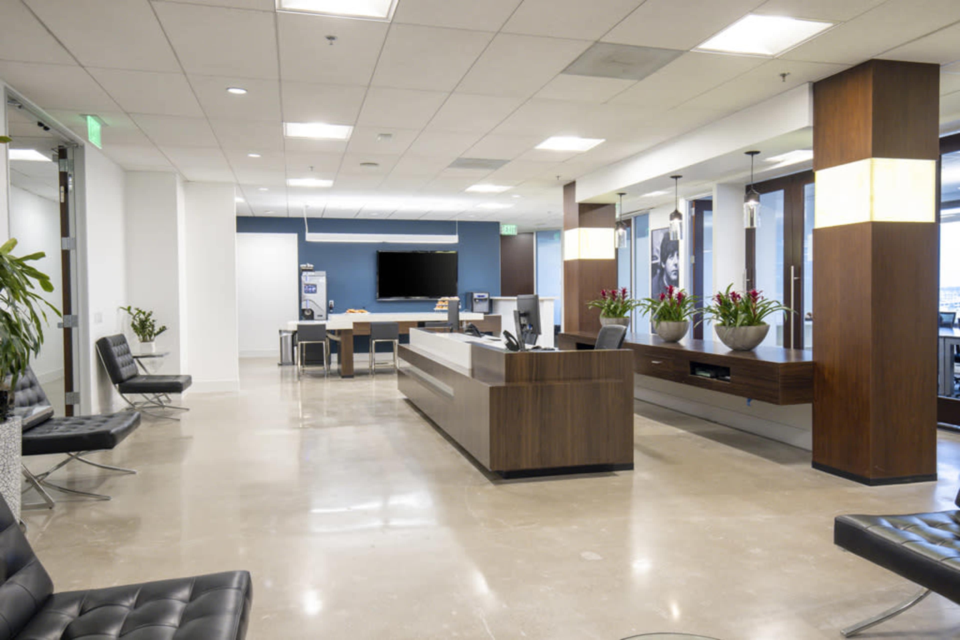 The image shows a modern office lobby with a reception desk, seating area, and tables arranged for meetings.