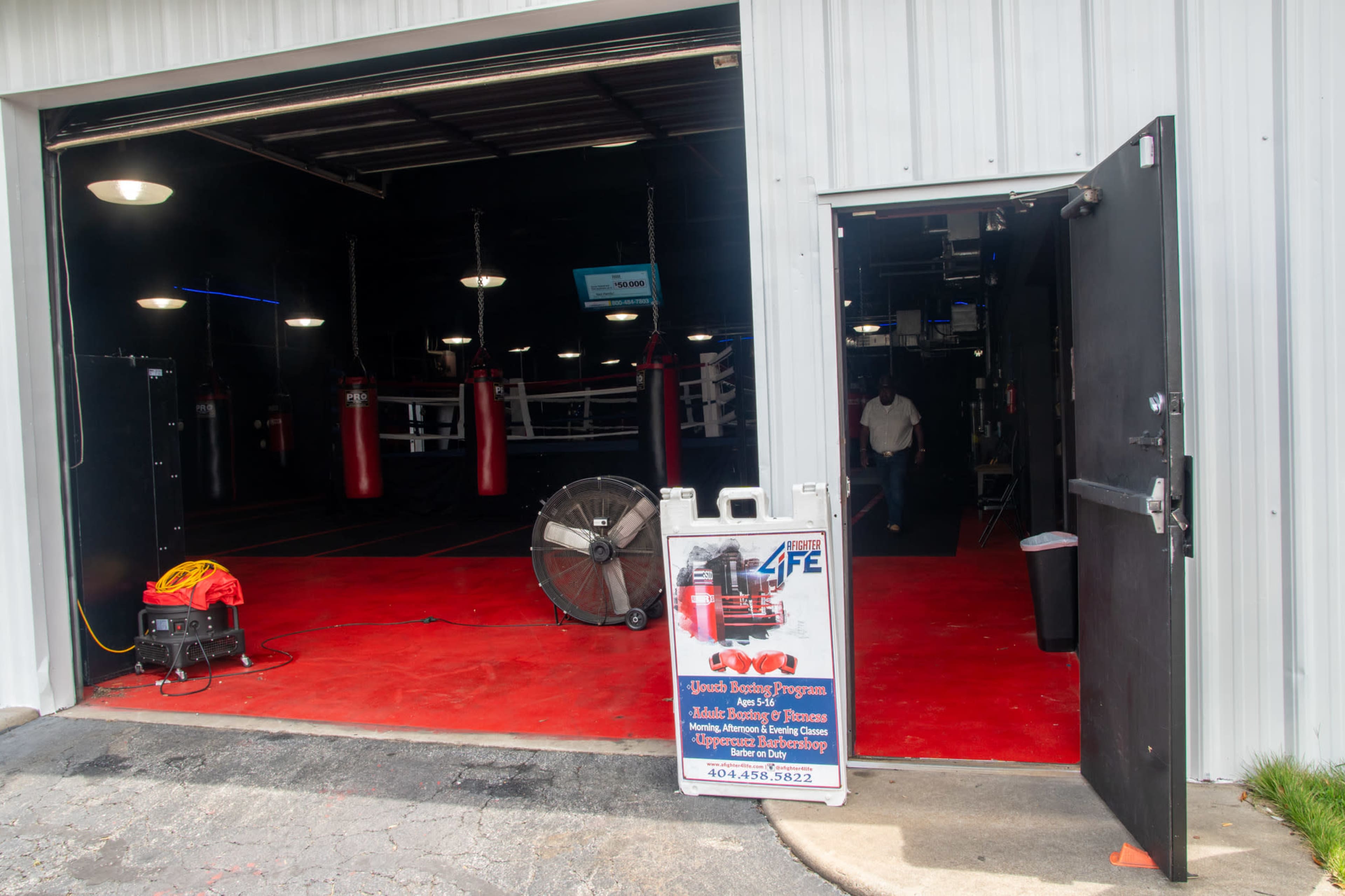 The image shows an open gym entrance with a sign advertising a boxing program and red punching bags lining the interior of the facility.