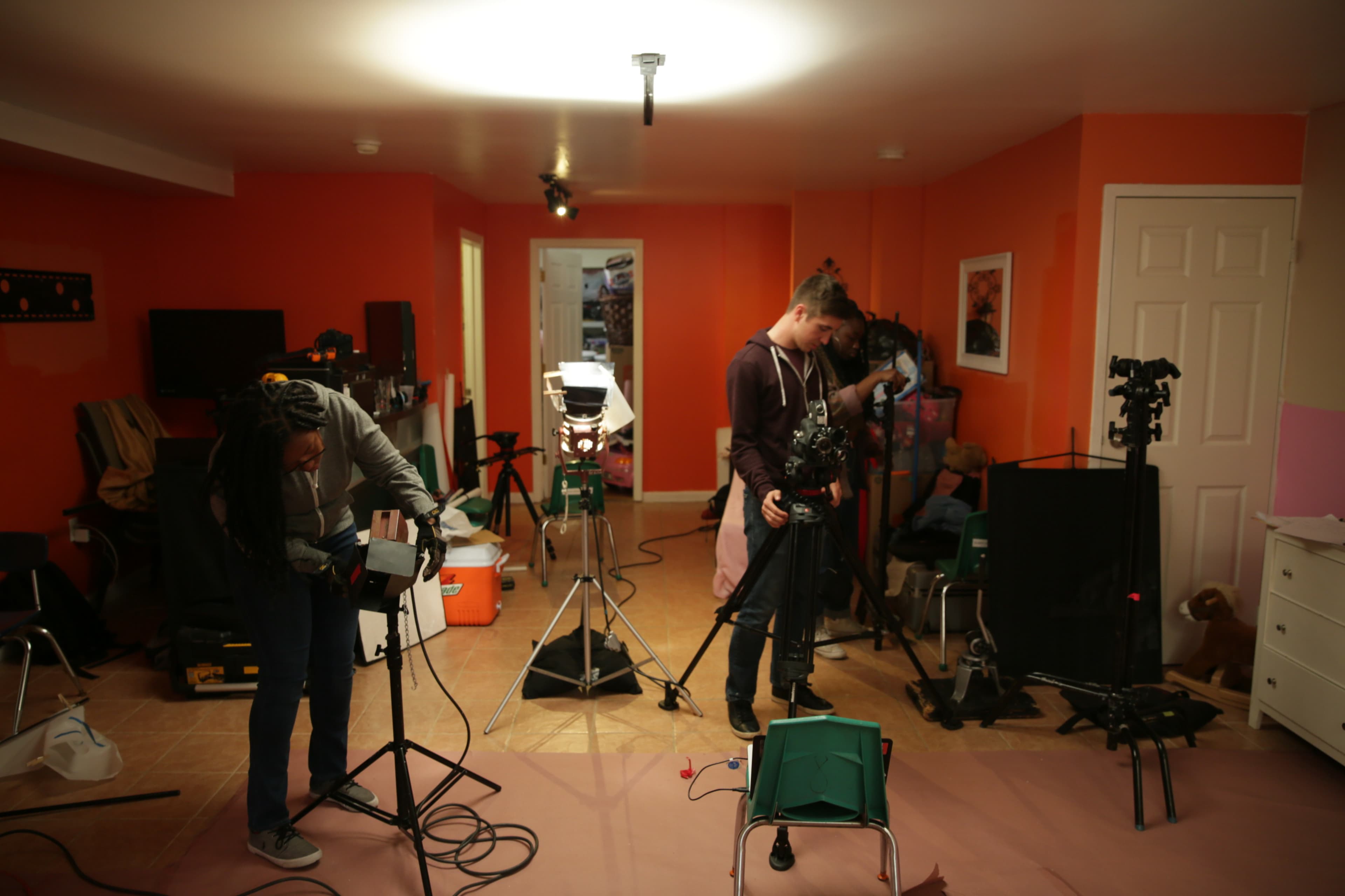 Two individuals are setting up filming equipment in a brightly colored room.