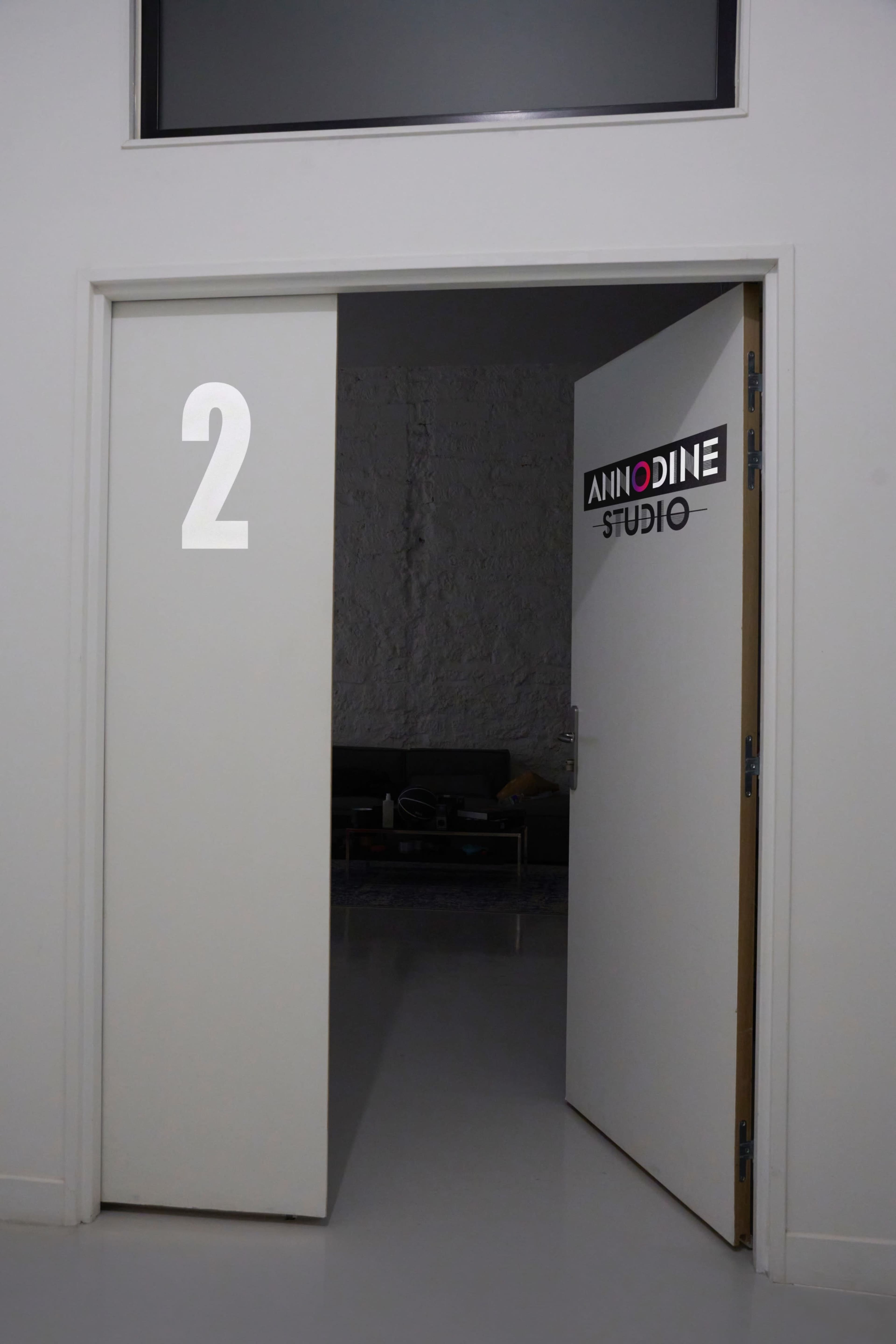 A white door with the number "2" and a sign reading "ANNODINE STUDIO" opens into a room with a visible seating area.