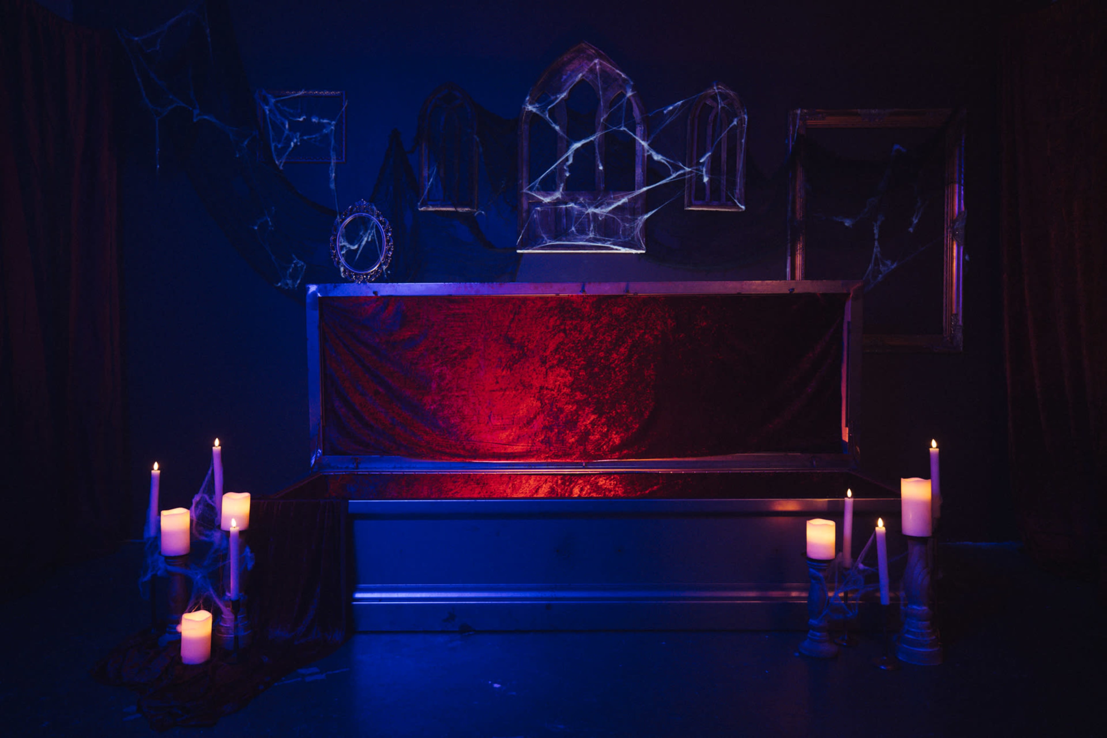 The scene features a dimly lit room with a velvet-draped bench, surrounded by lit candles and cobwebs, with ghostly mirrors mounted on the dark walls.