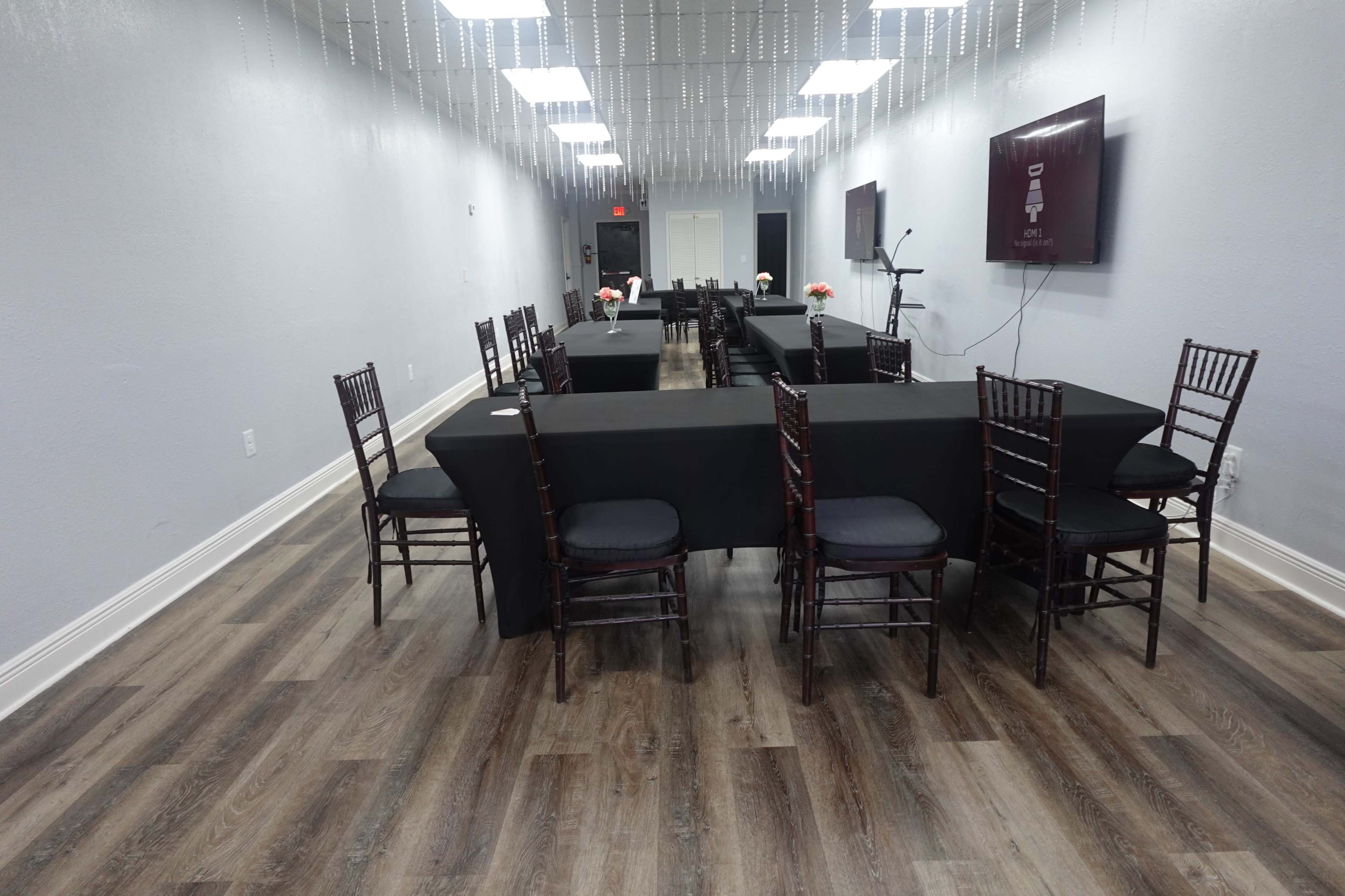 A long, narrow room set up for an event, featuring black tablecloths on several tables and chairs arranged around them, with floral centerpieces on the tables.