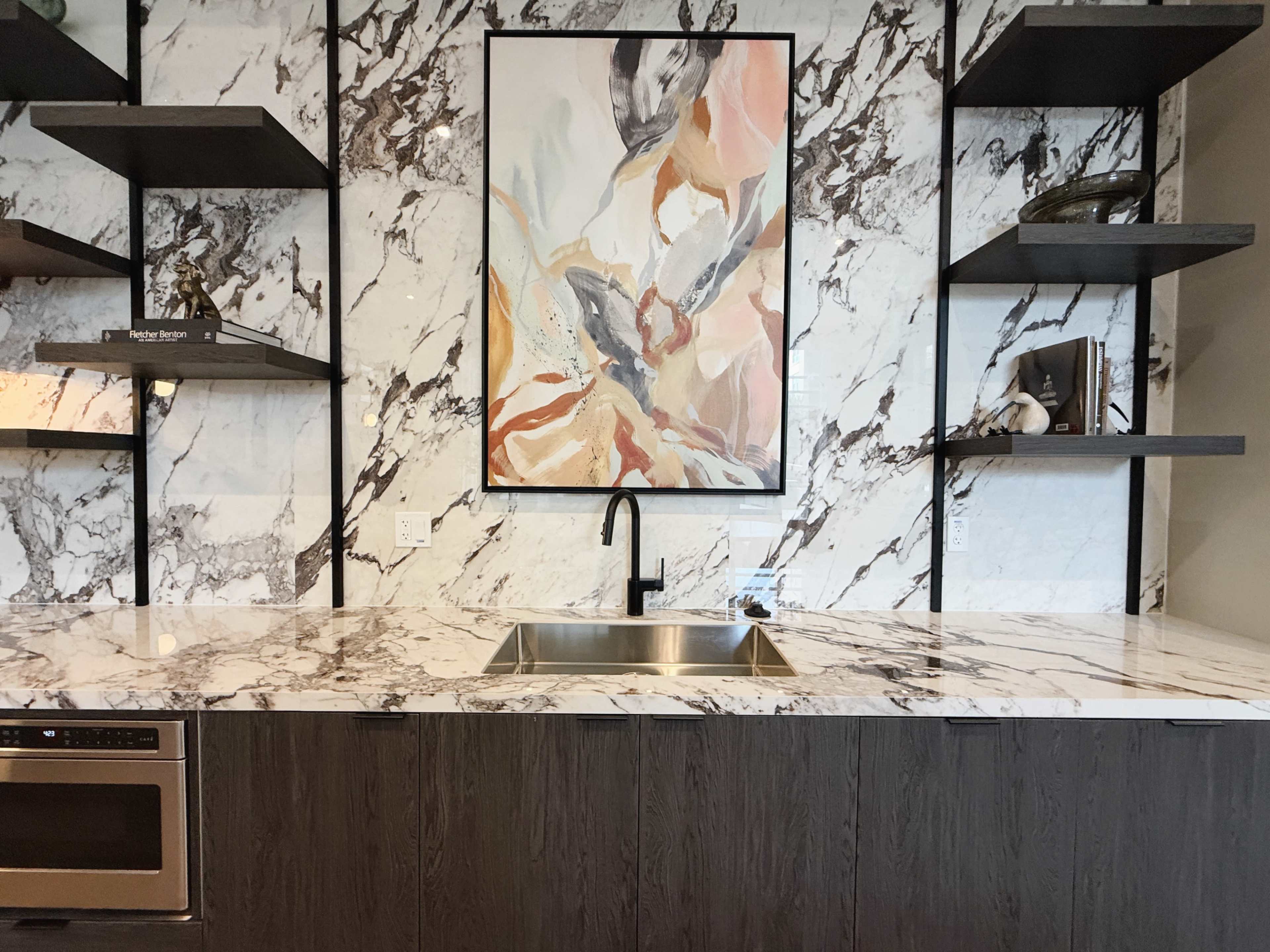 The image shows a modern kitchen with a marble backsplash, a central sink, and open shelving above dark wood cabinets.