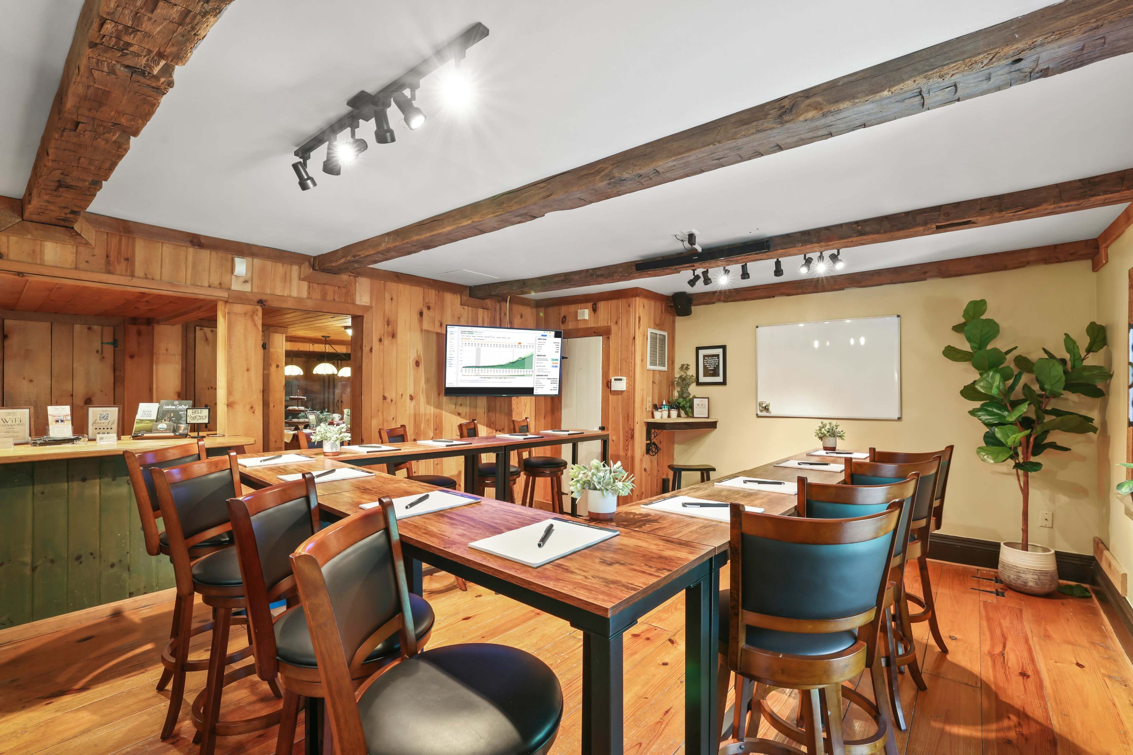 A well-organized meeting room with wooden beams, a large screen for presentations, and tables arranged with chairs around them.