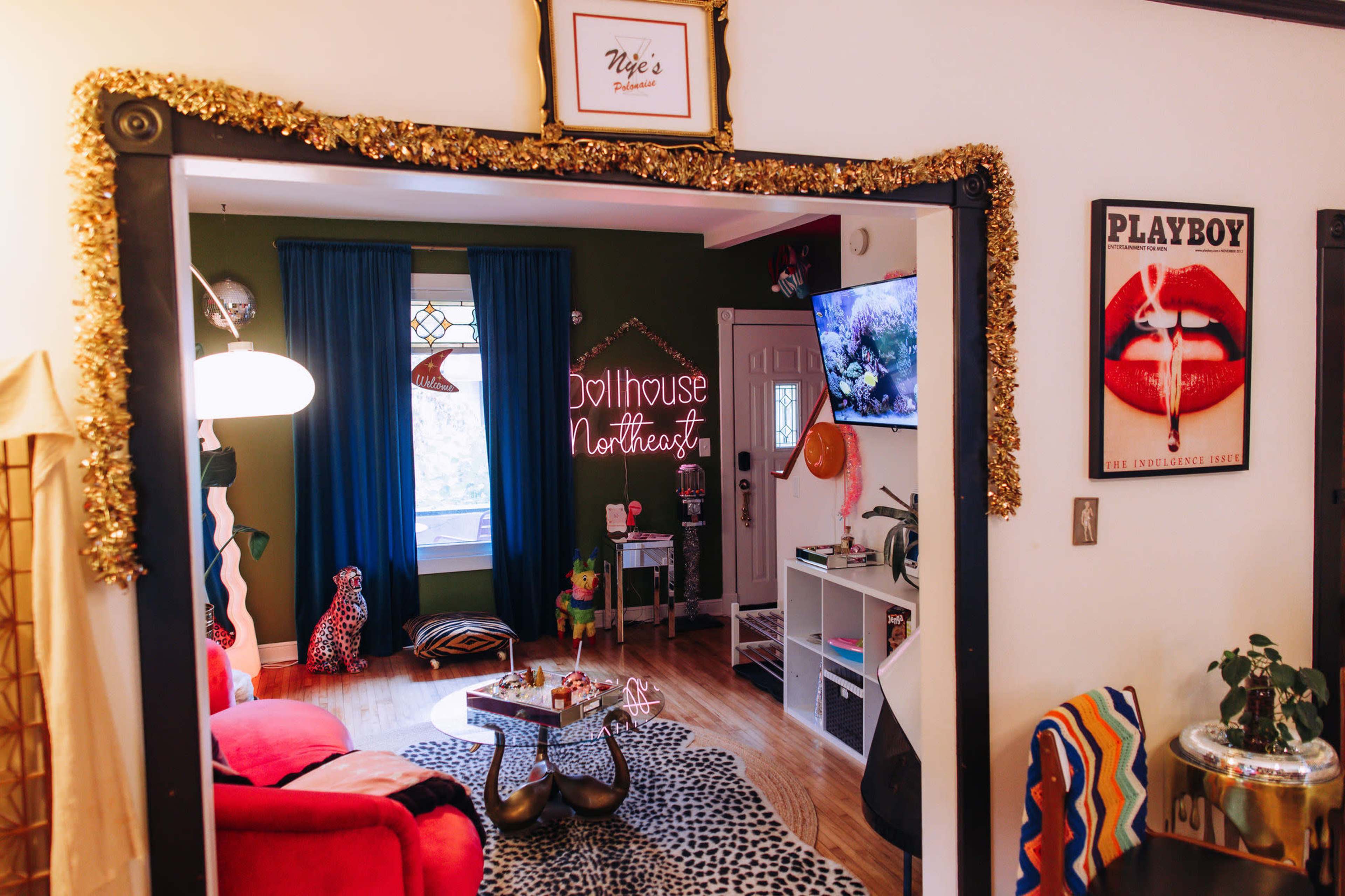 A cozy living room features colorful decor, including a red couch, playful artwork, and a television, framed by a decorated doorway.