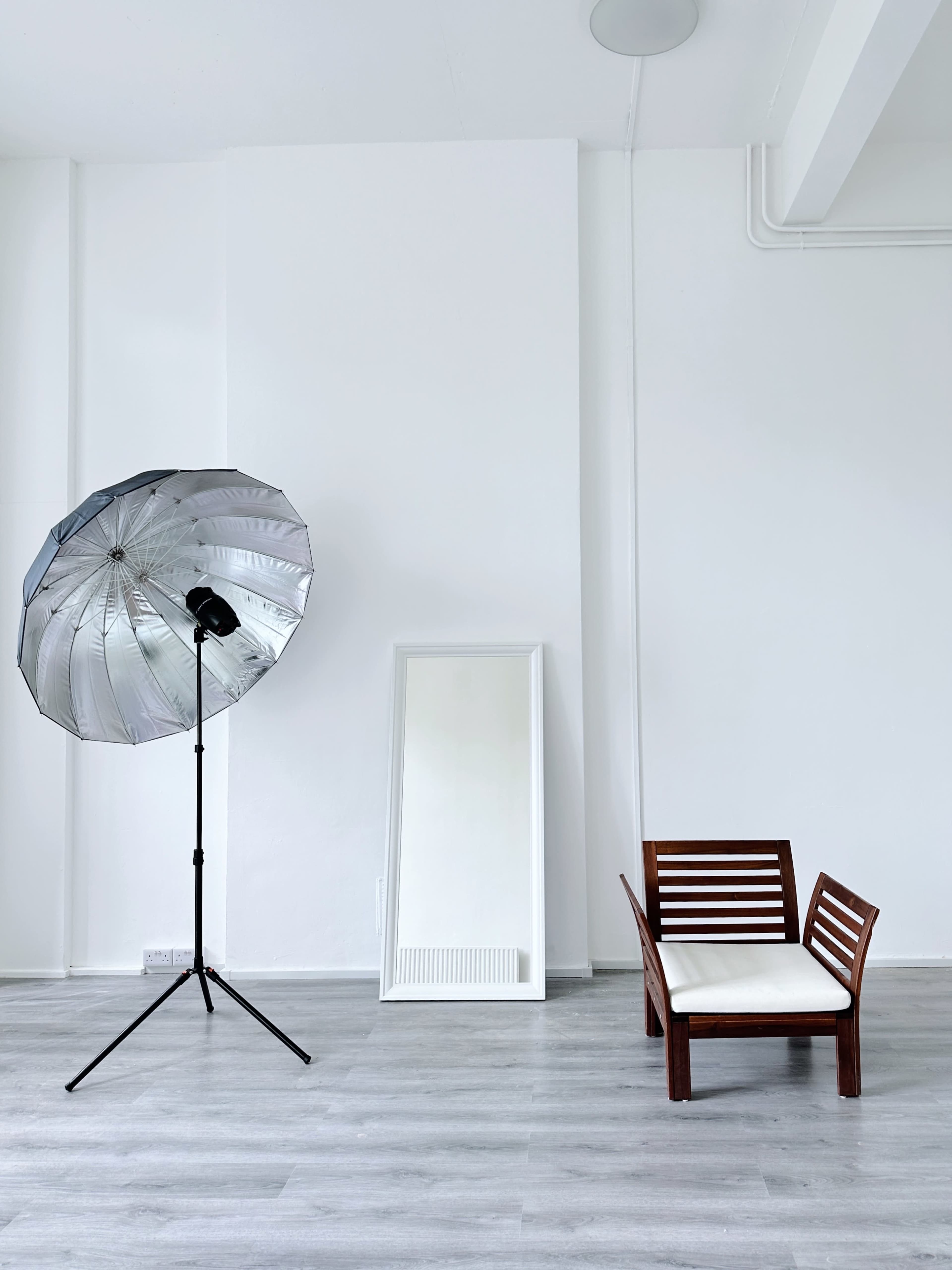 A minimalistic interior with a large umbrella light, a full-length mirror, and a wooden chair against a white wall.