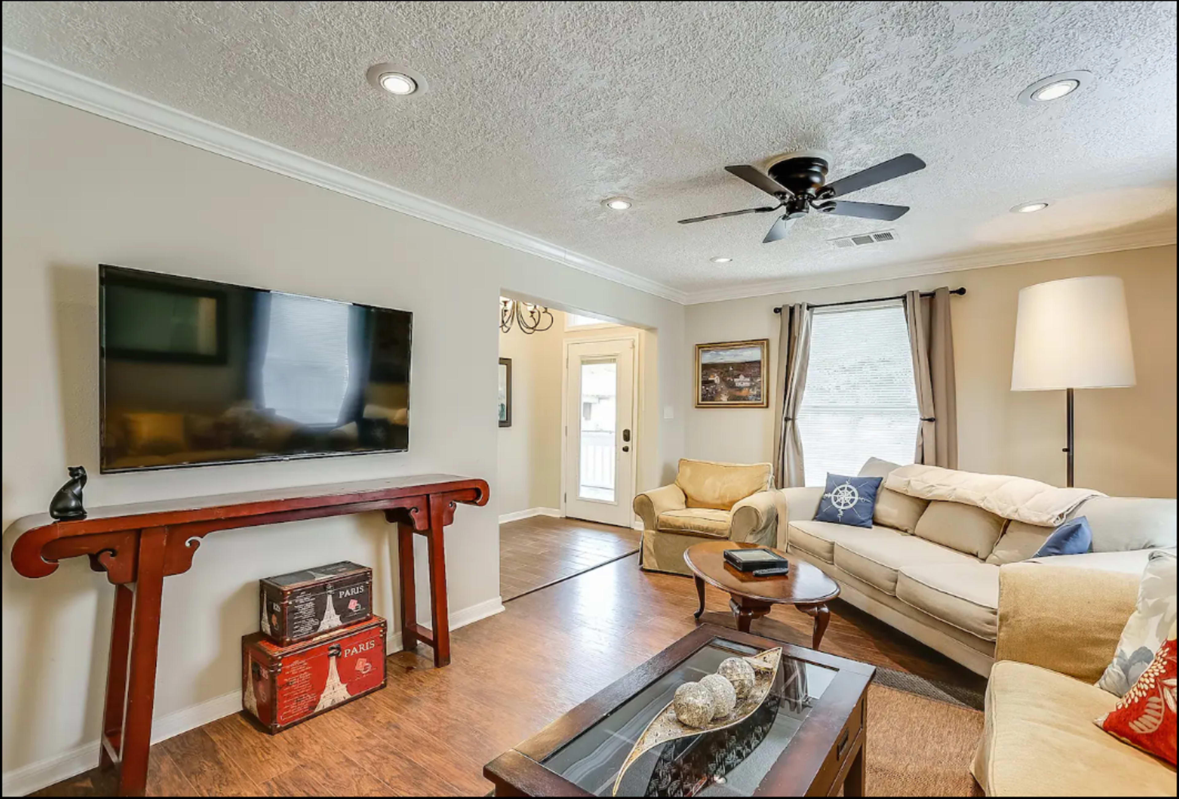 A living room with a television mounted on the wall, a sofa, a coffee table, and a door leading outside.