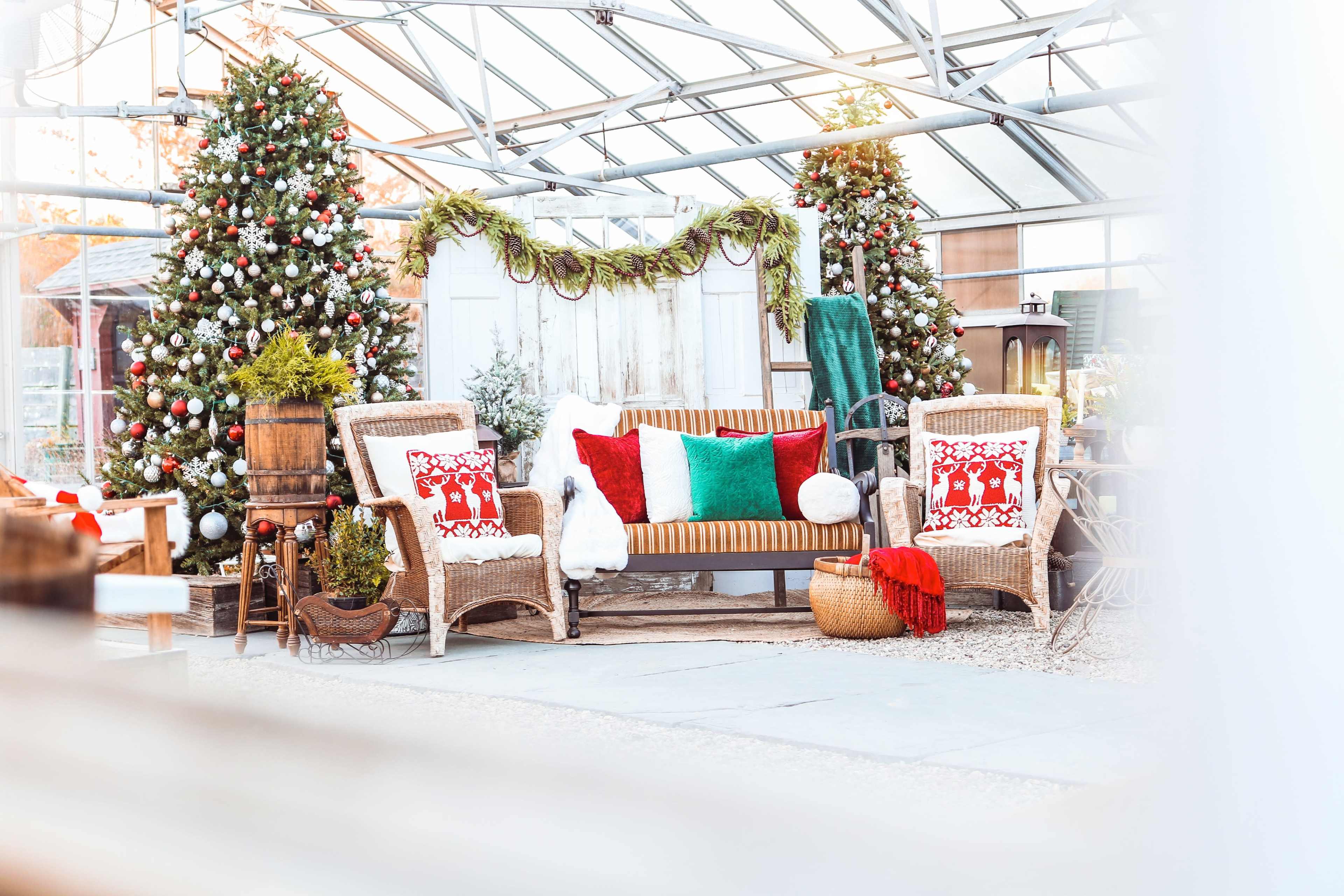The scene features a cozy greenhouse decorated for the holidays, with two Christmas trees, a rustic sofa, and festive cushions.