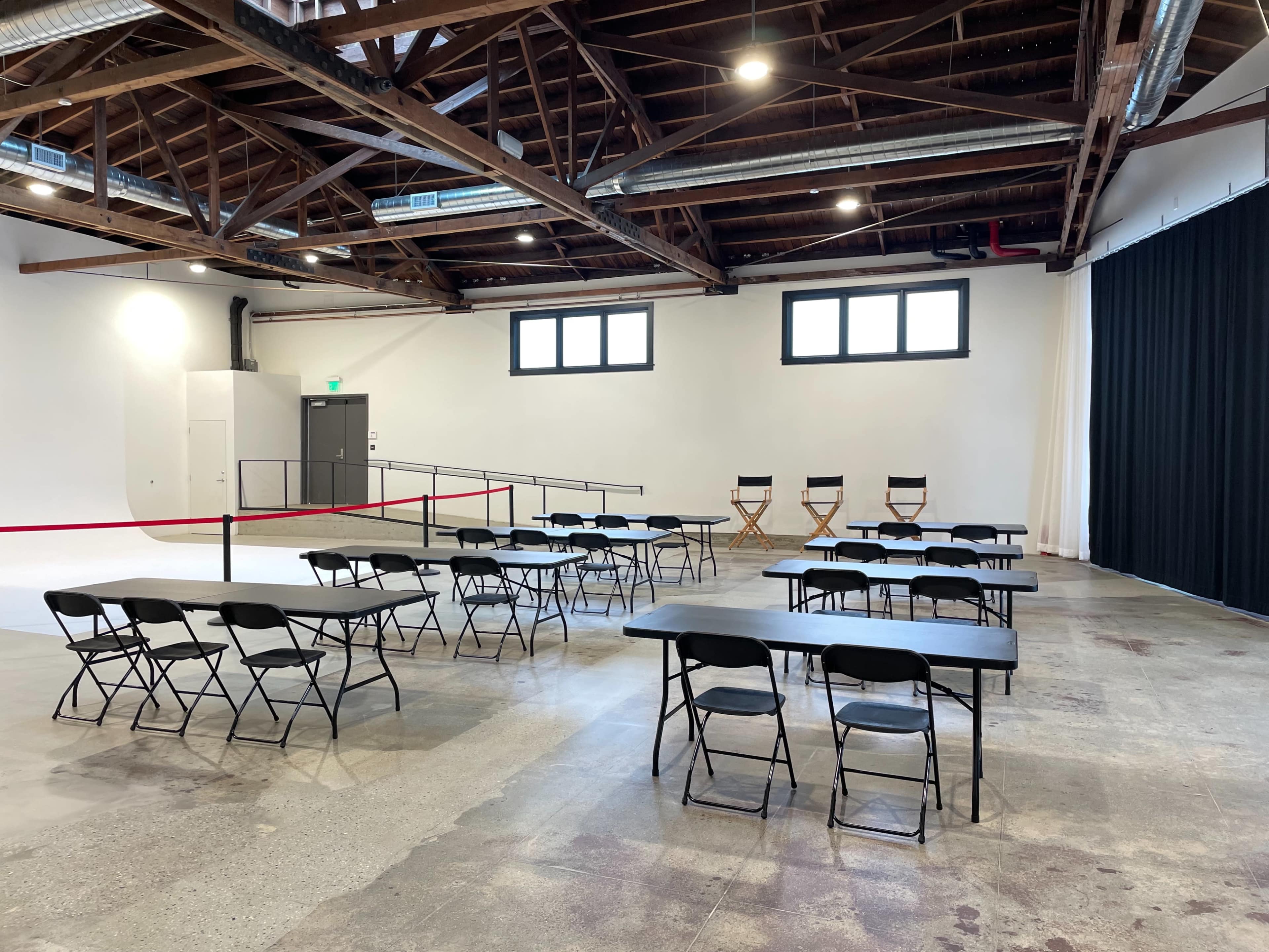 A spacious room with several rows of black folding tables and chairs, along with three director's chairs against one wall.