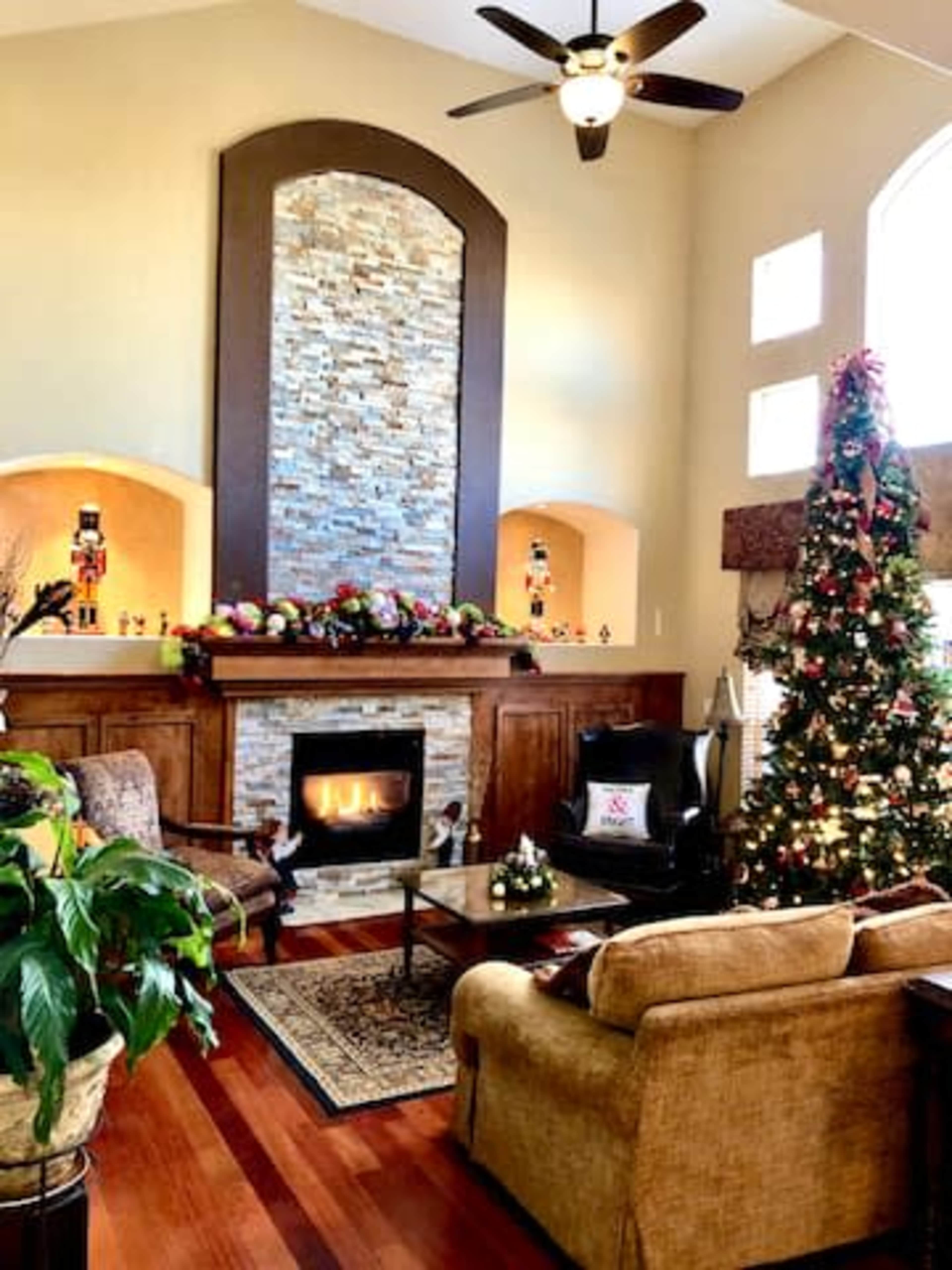 The living room features a stone fireplace with a mantel decorated for the holidays, a Christmas tree, and seating arranged around a coffee table.