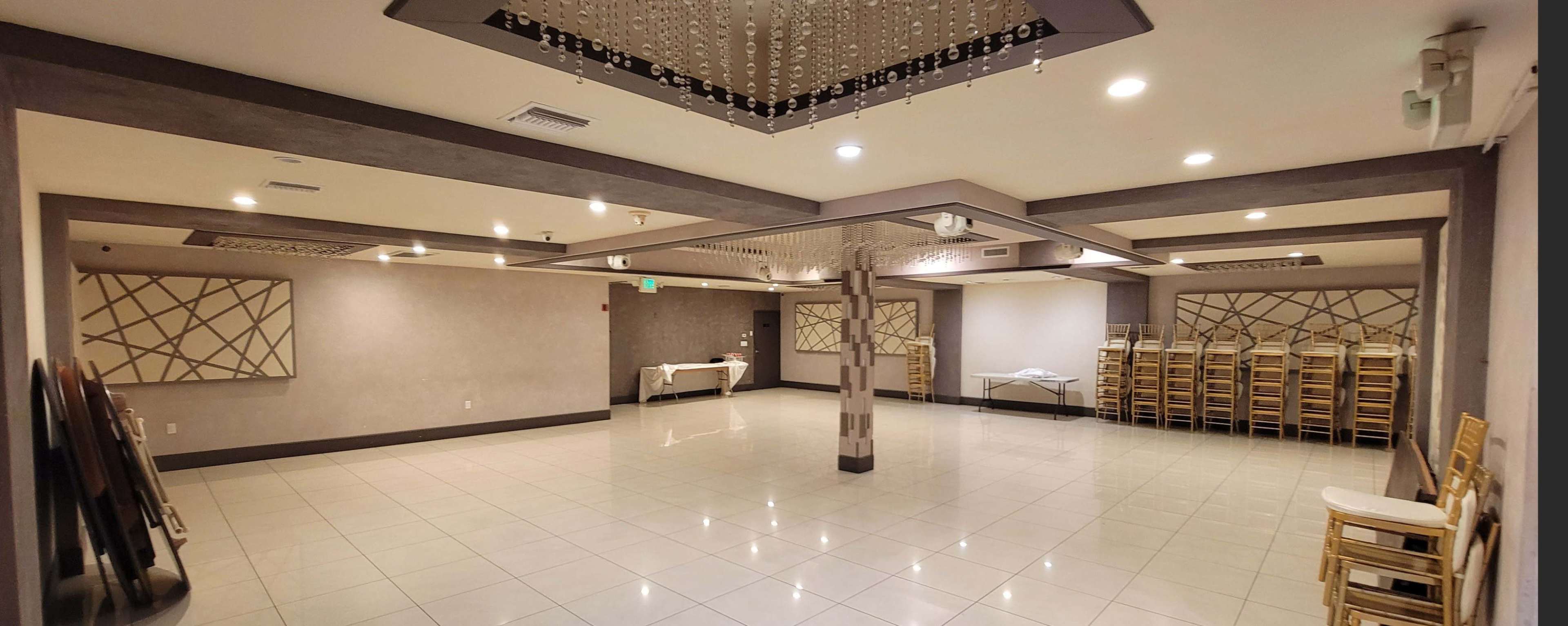 The image shows a spacious, empty reception hall with tiled flooring, dim lighting, and stacked chairs against the wall.
