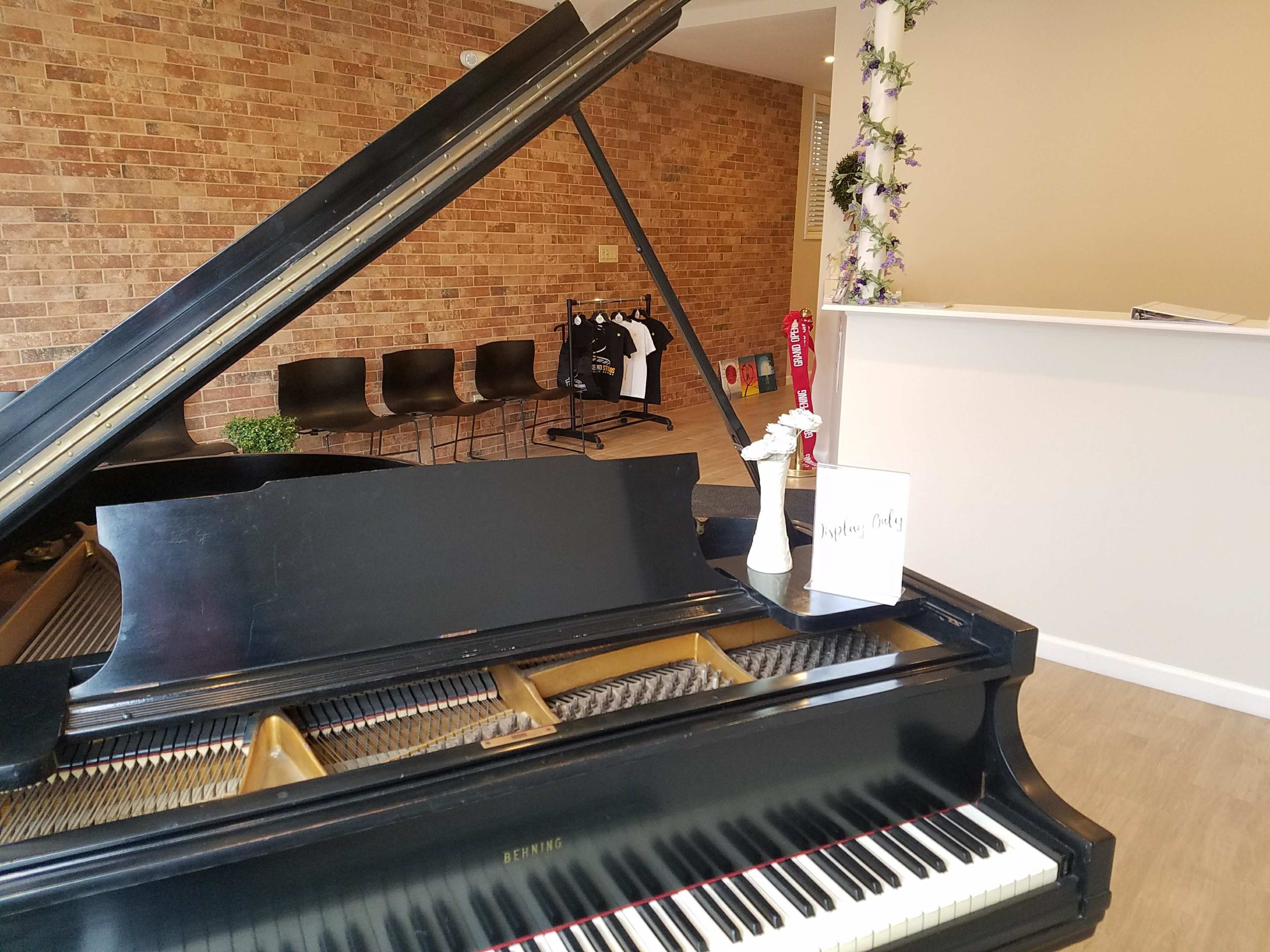 A grand piano is positioned in the foreground of a modern room with brick walls and a reception area featuring chairs and decor.