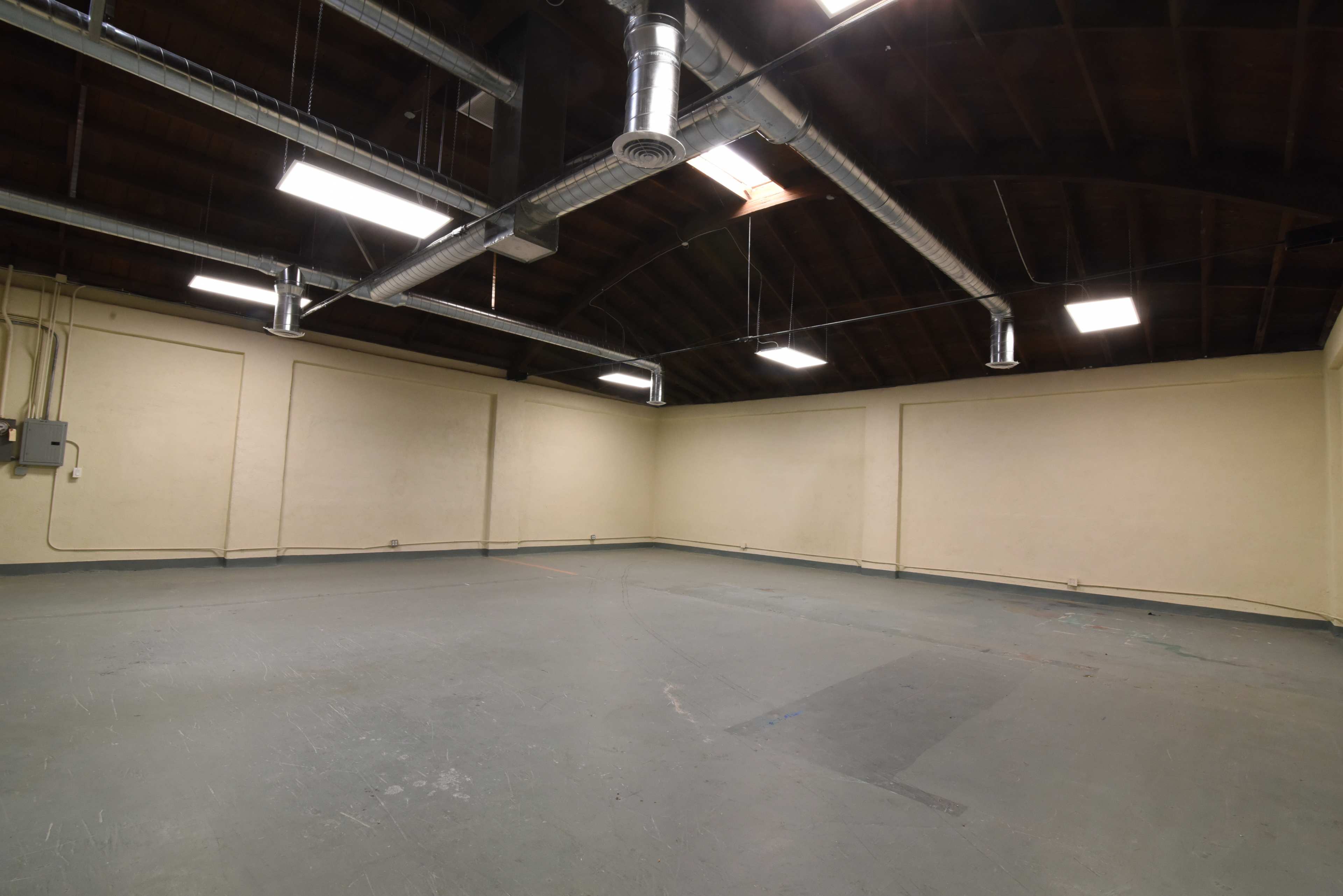 An empty room with high ceilings, exposed ductwork, and bare walls.