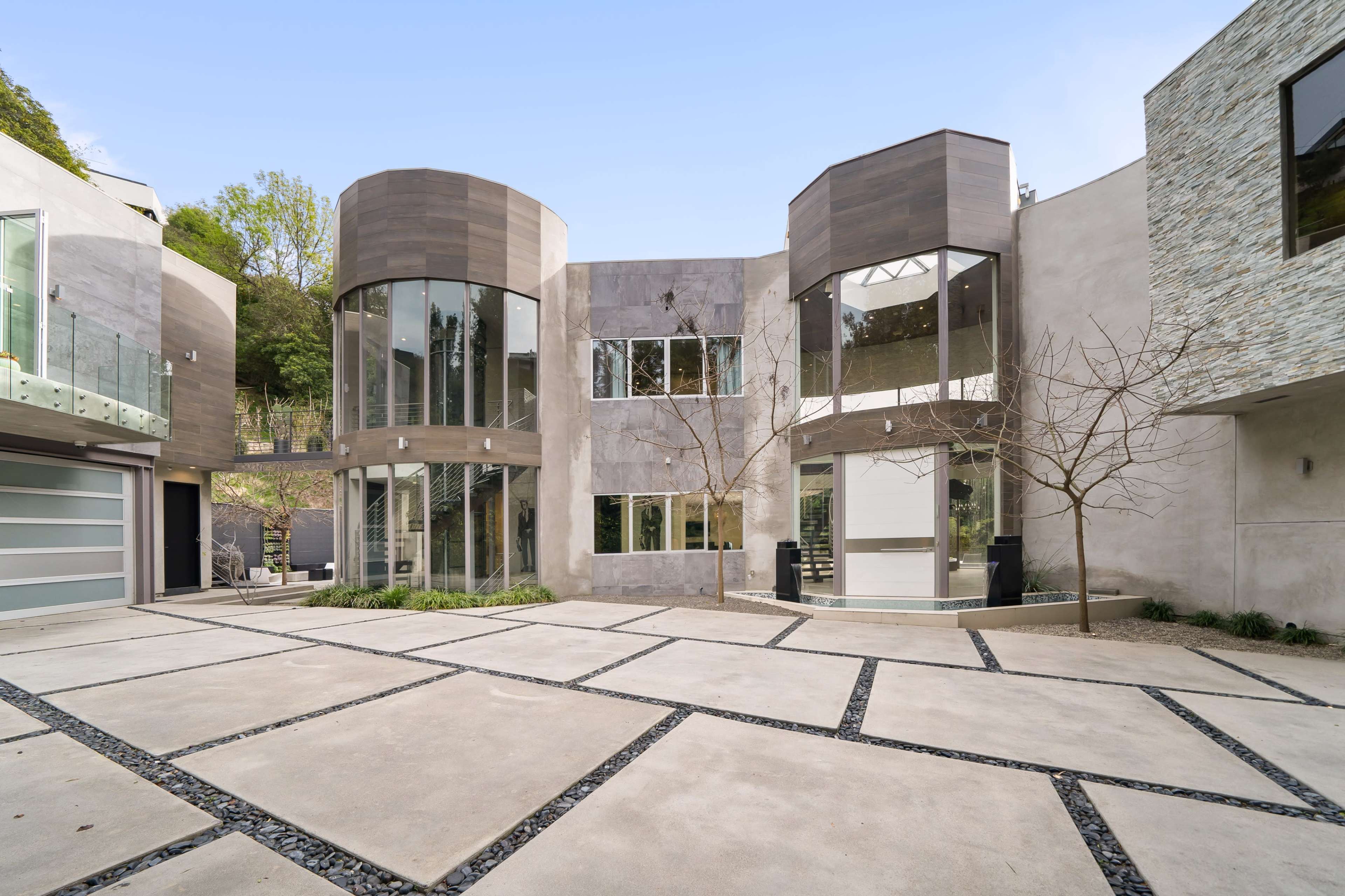 A modern, multi-level home with large glass windows and a minimalist courtyard featuring geometric stone pathways.