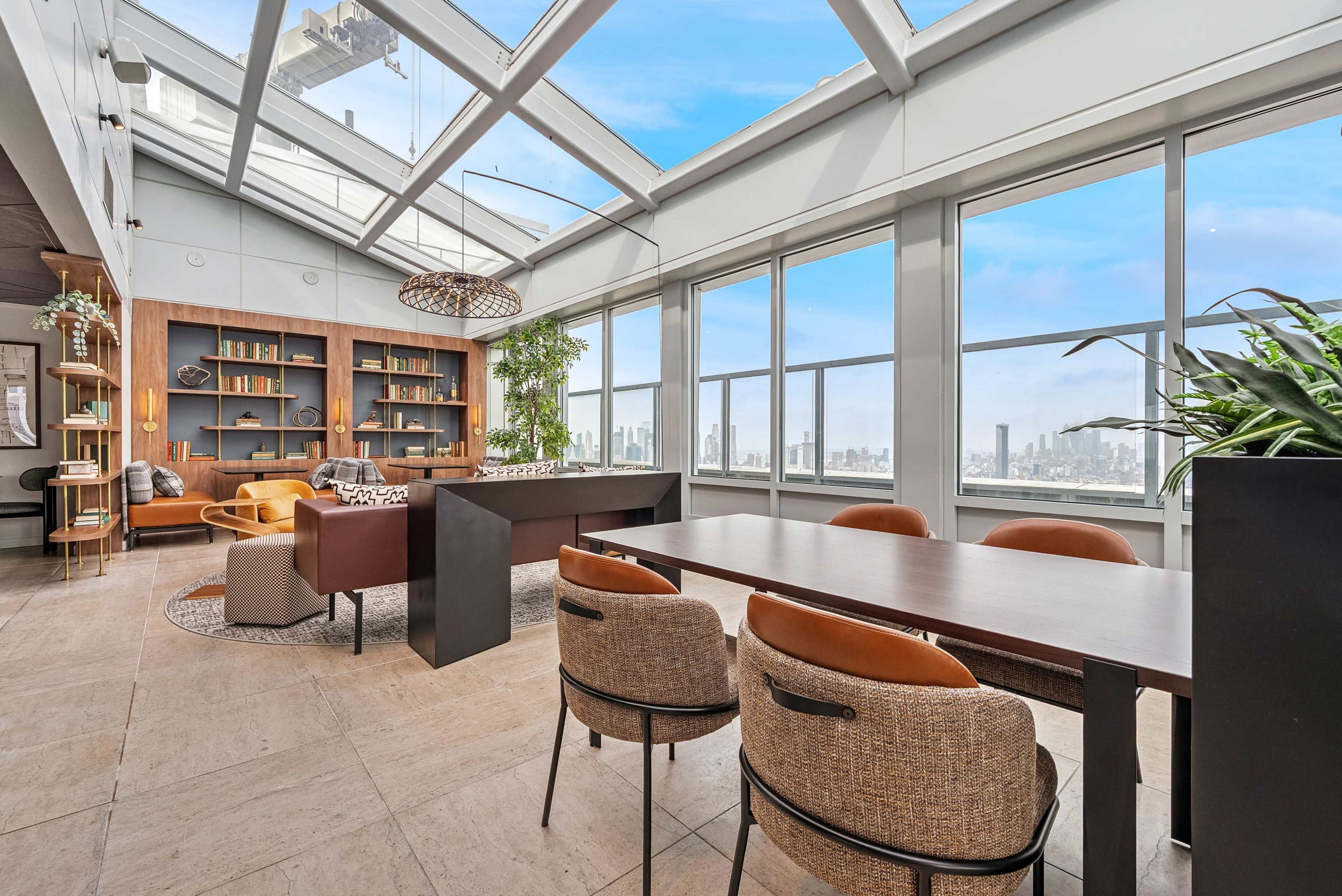 The image shows a modern penthouse interior with large windows, a dining area, and a city skyline view.