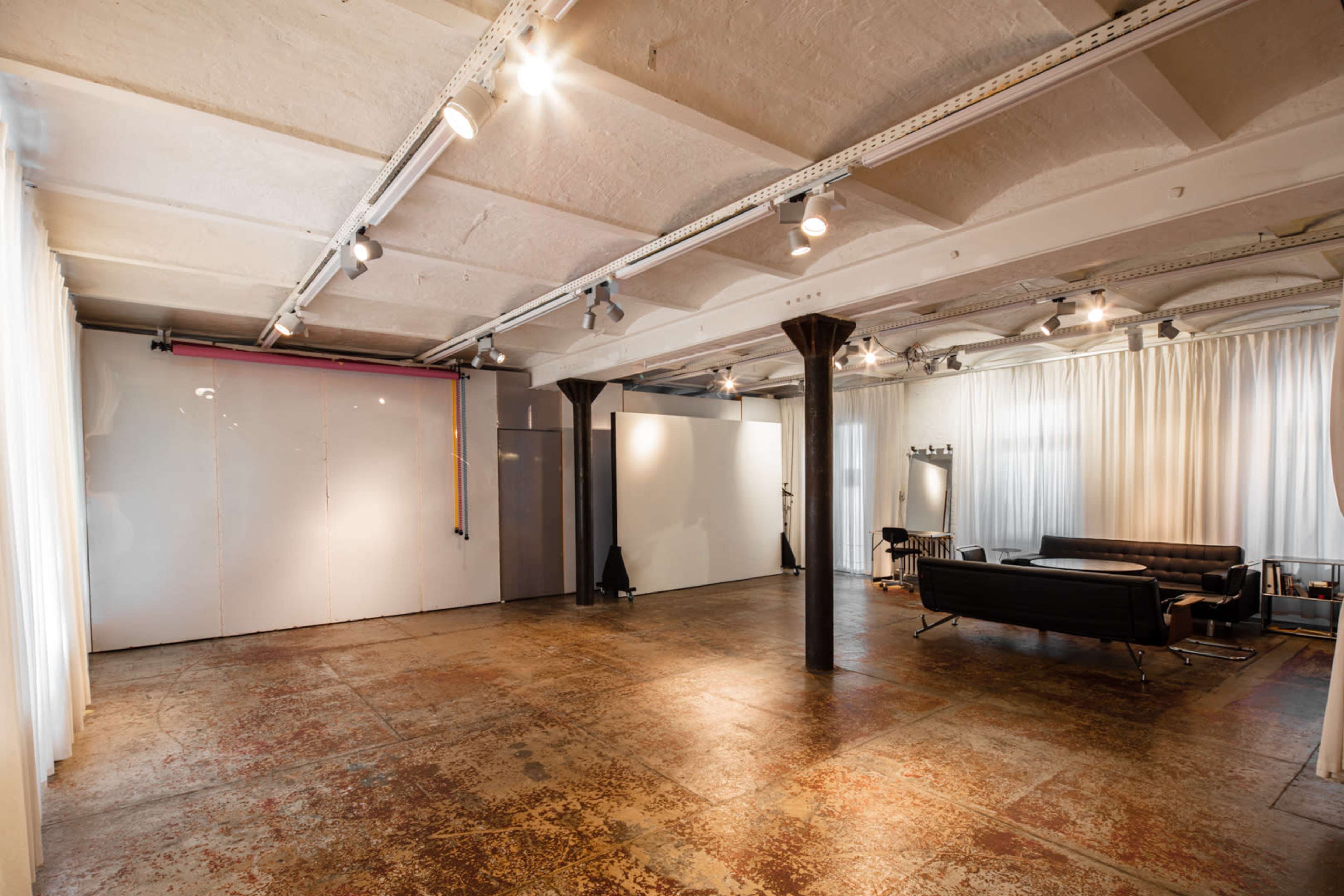 The image depicts a spacious, industrial-style room with polished concrete flooring, white walls, and large windows draped with sheer curtains.