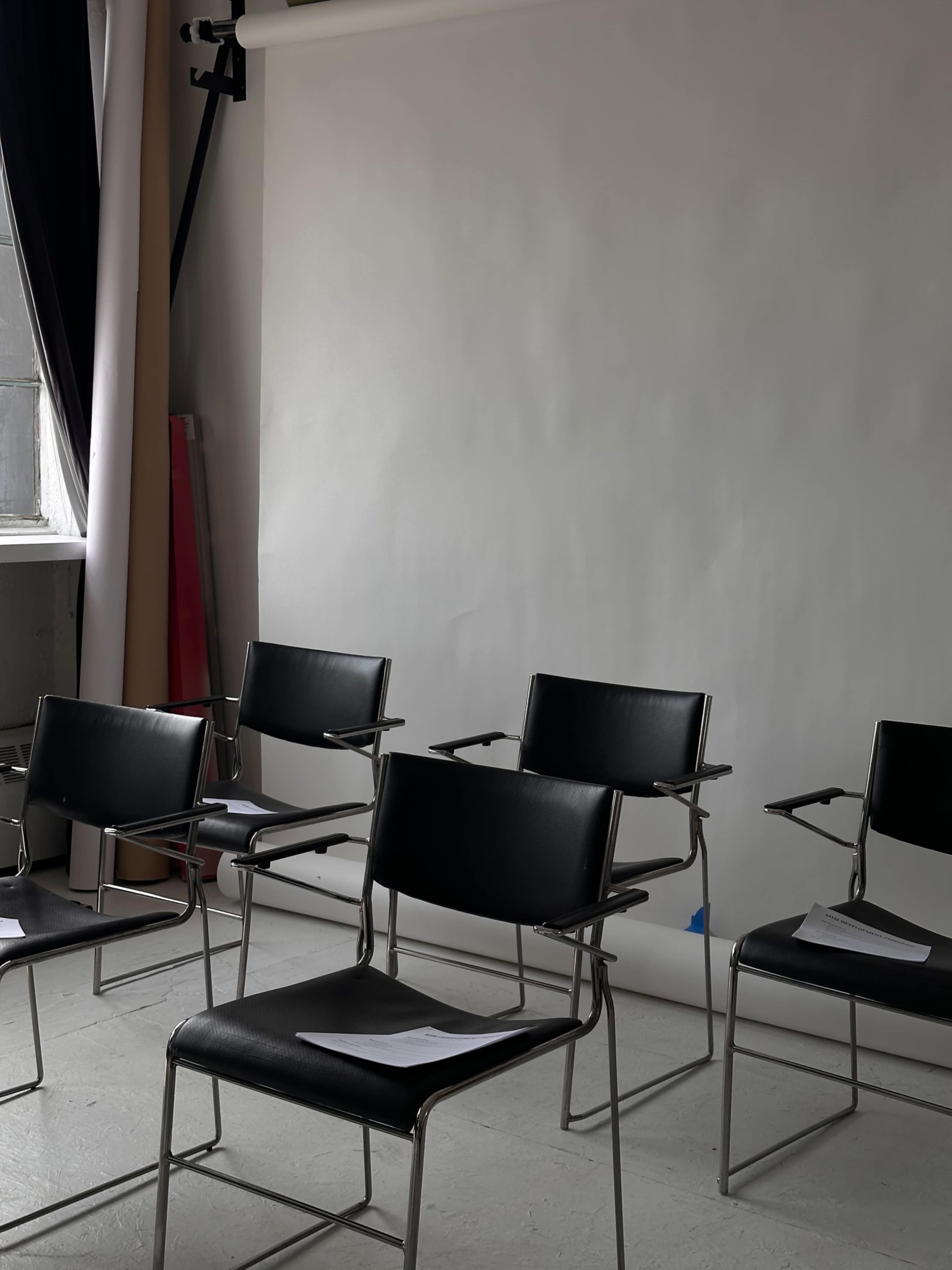 The image features several black metal-framed chairs arranged in a studio space with a plain white backdrop.