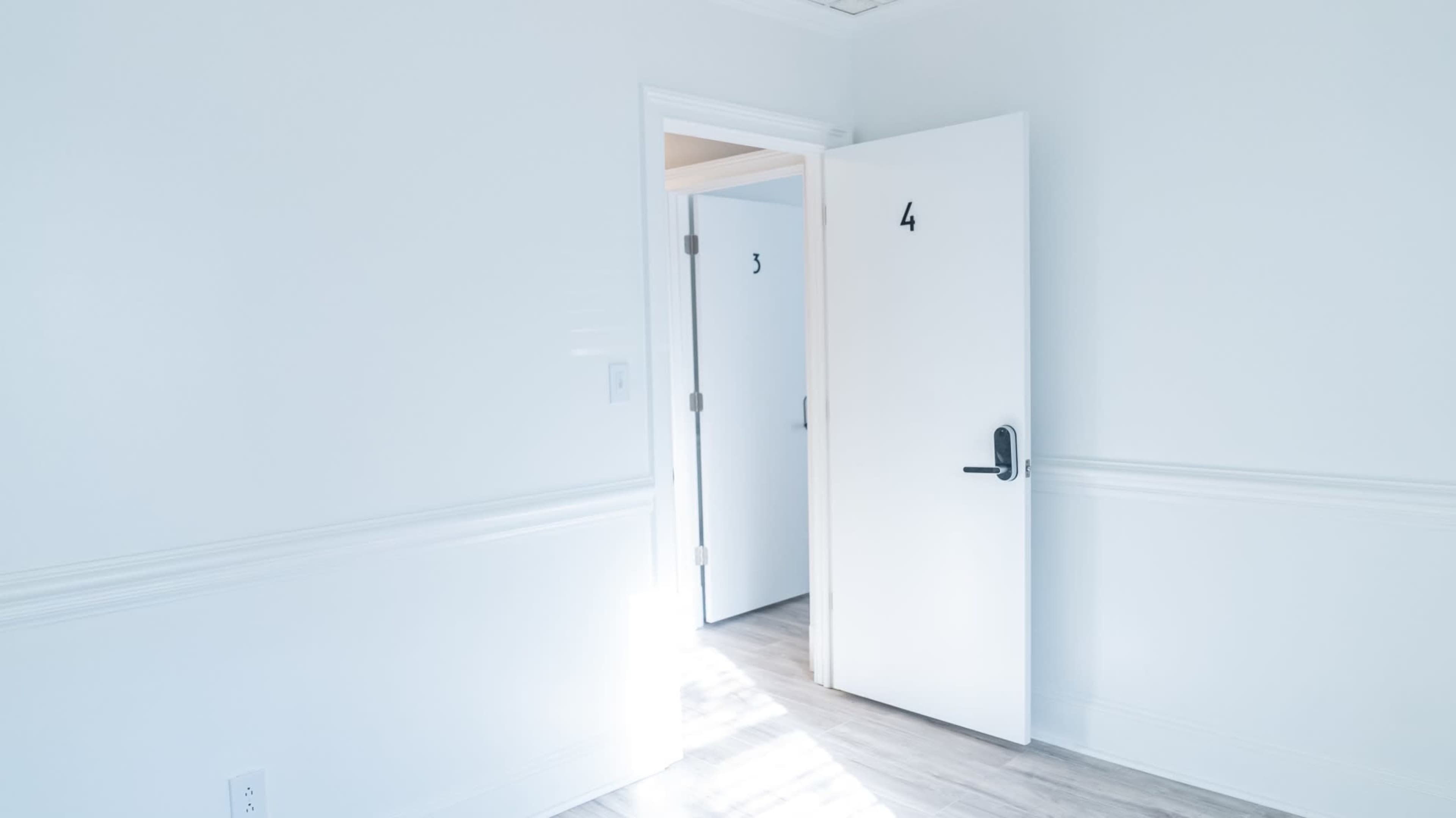A bright room with light-colored walls features two doors, one partially open with the number 4 and the other labeled with the number 3.
