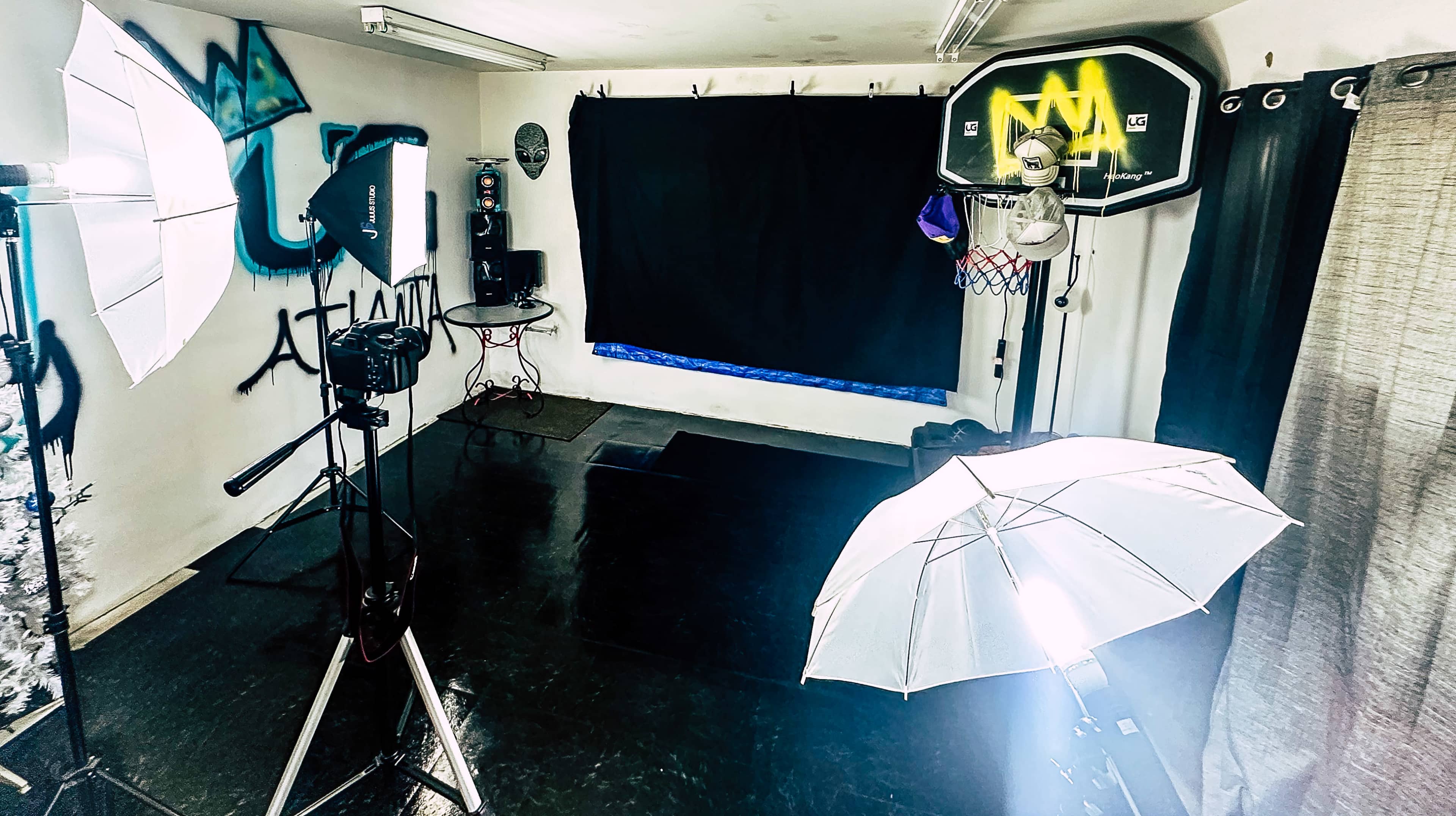 A dimly lit indoor space set up for photography or filming, featuring a black backdrop, lighting equipment, and a basketball hoop.