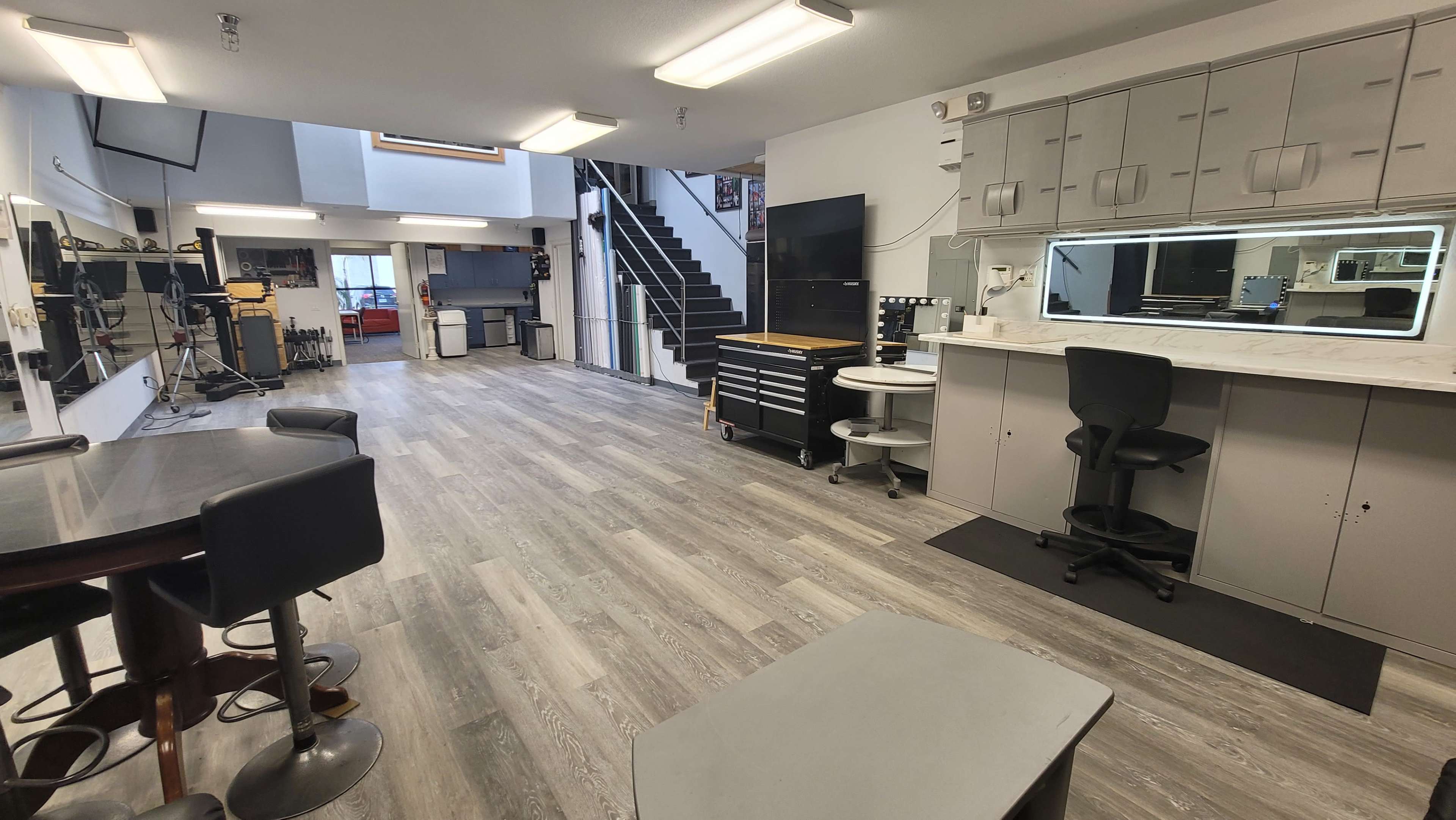 A spacious, modern studio with a kitchen area, workstations, and a staircase in the background.