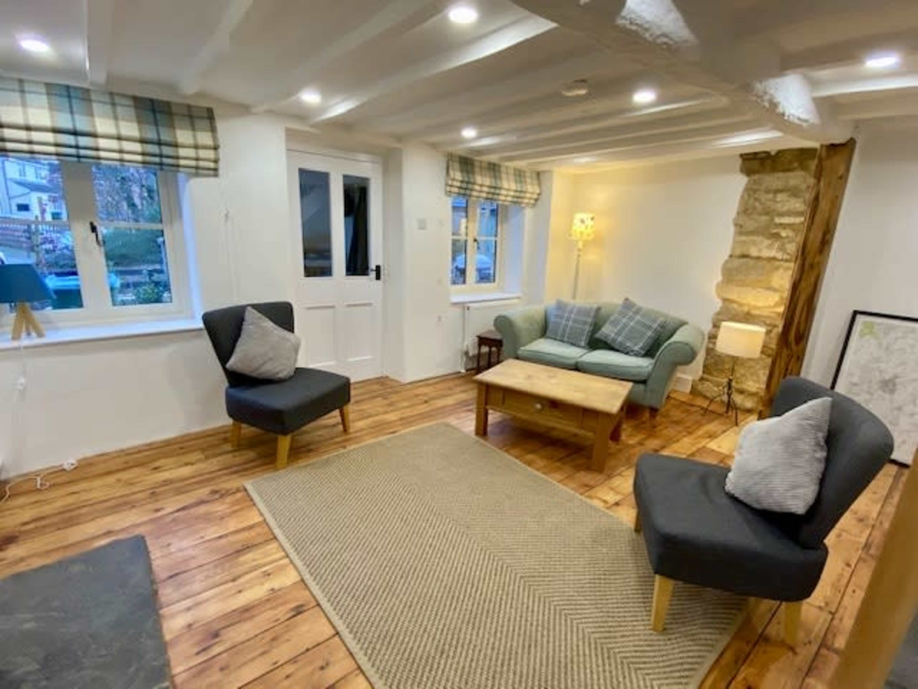 A cozy living room with a light wooden floor, a green sofa, two armchairs, a coffee table, and a stone wall feature.