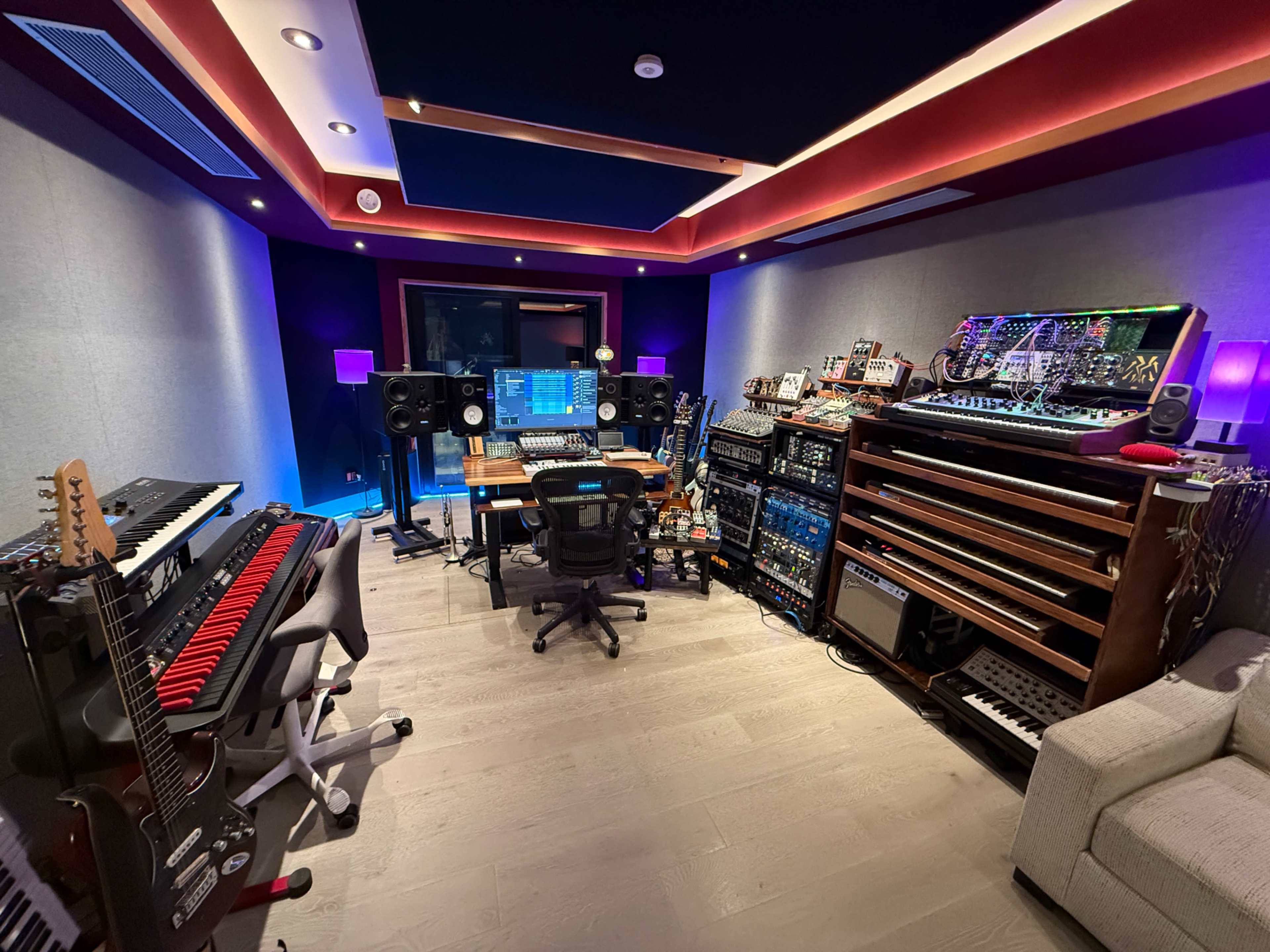 The image shows a well-equipped music production studio featuring various instruments, sound equipment, and a central workstation.