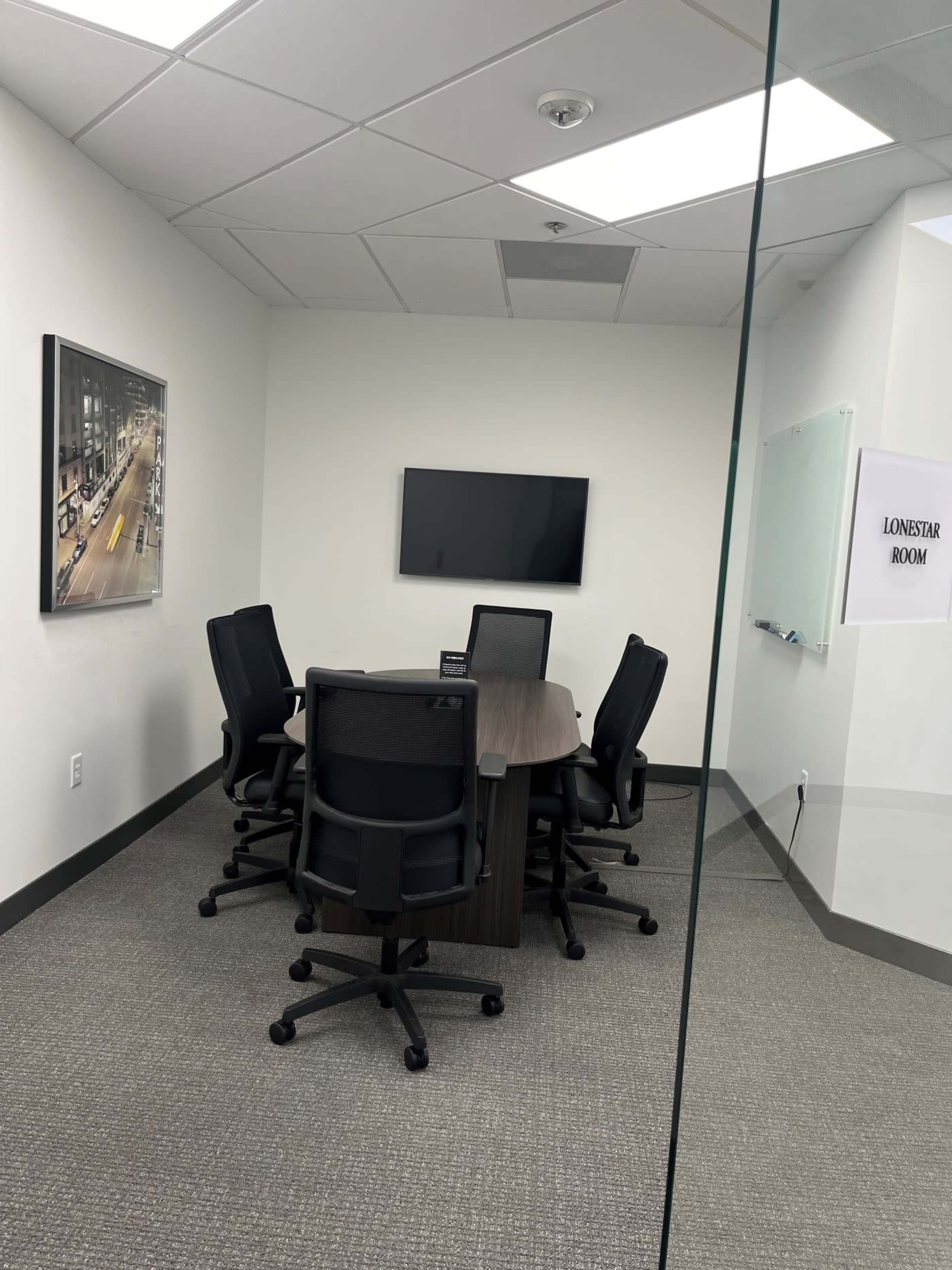 The image shows a conference room with a large table, six office chairs, a wall-mounted television, and a glass partition with a sign indicating "LONESTAR ROOM."