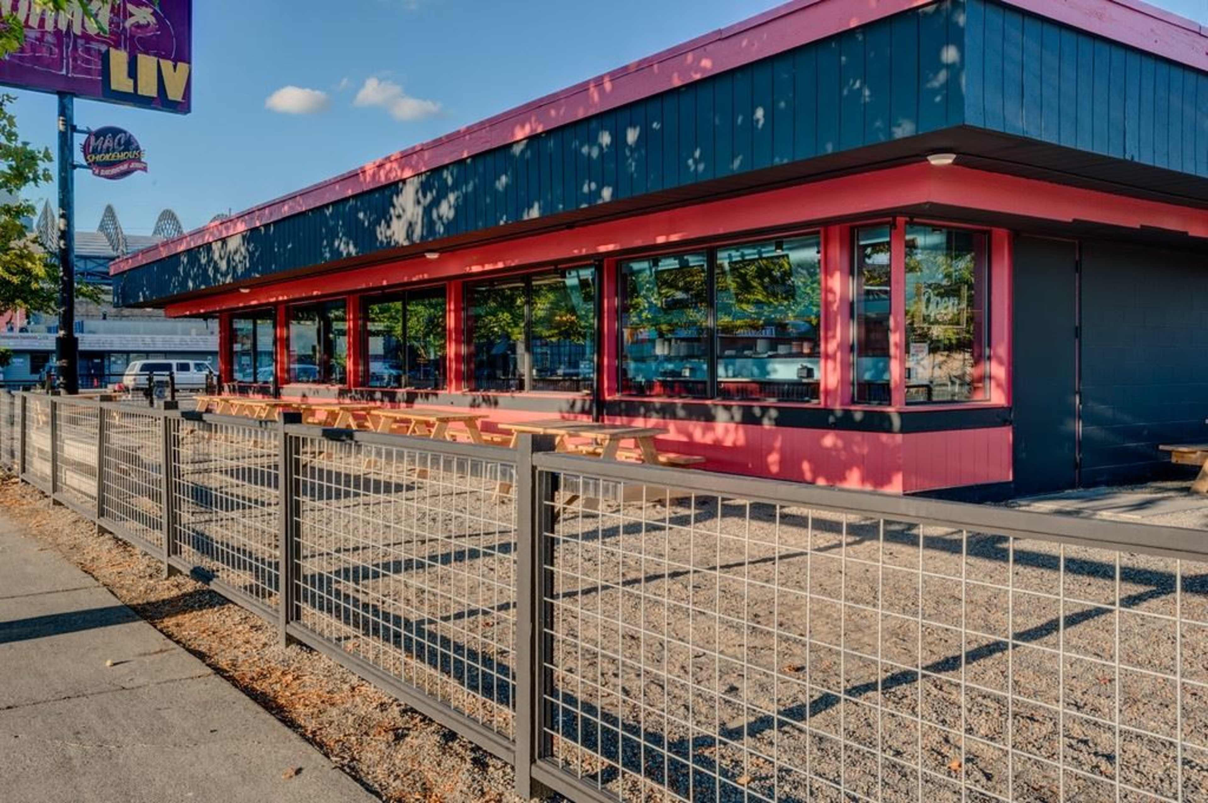 A modern restaurant with large windows and a pink exterior features outdoor seating enclosed by a fence.