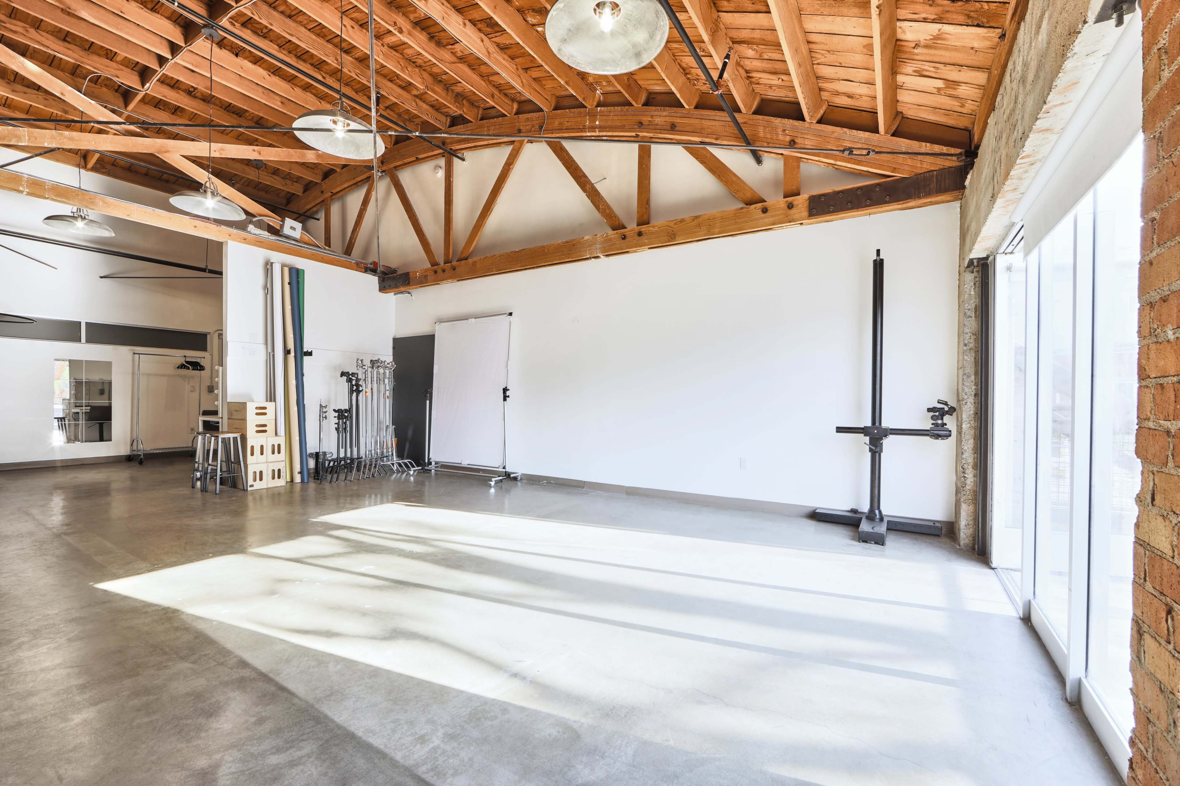 A spacious studio with high wooden beams, large windows, and concrete flooring, equipped with various photography gear.