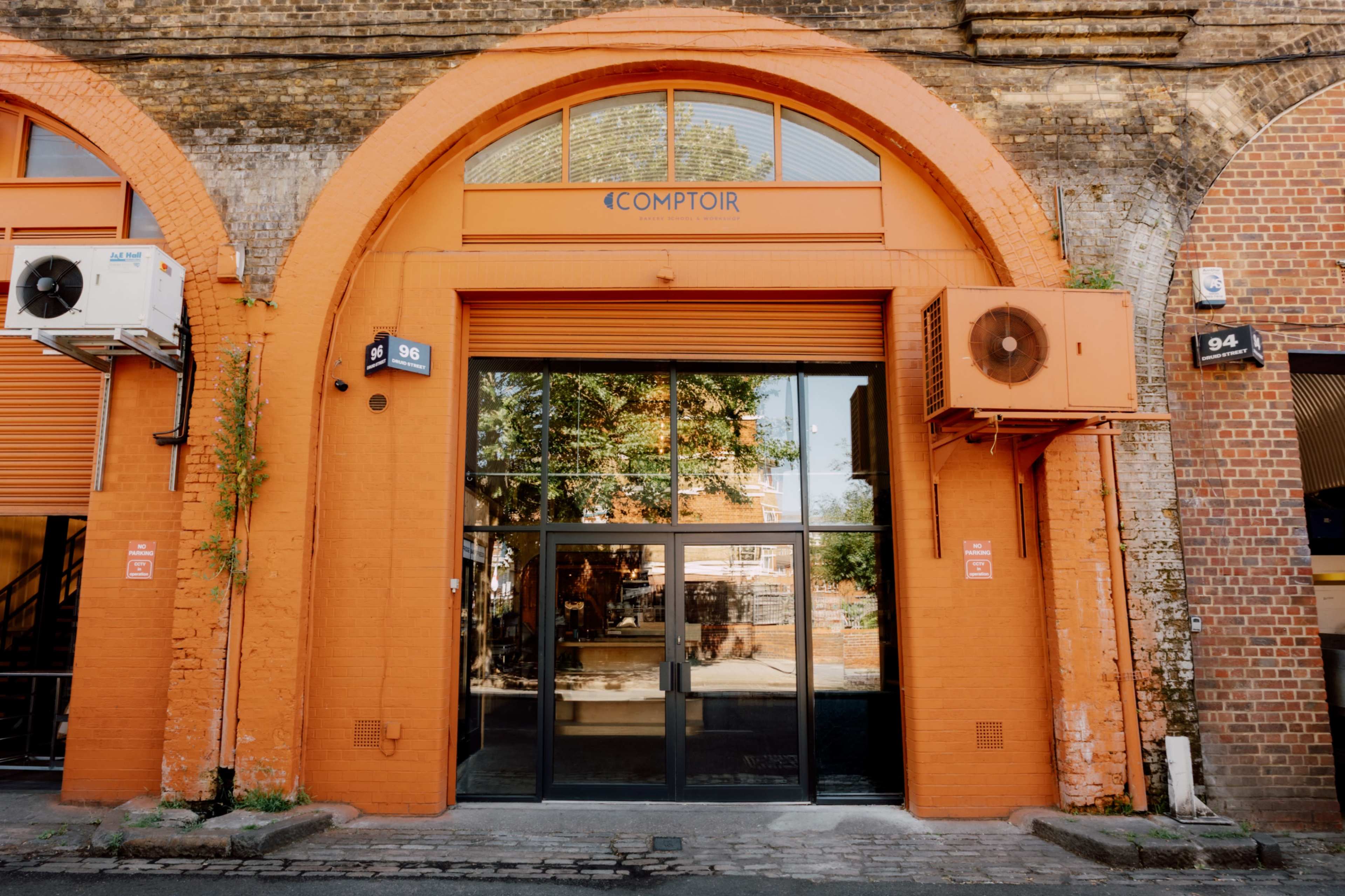 The image shows an orange-painted building with large glass doors, air conditioning units on either side, and the word "COMPTIOR" displayed above the entrance.