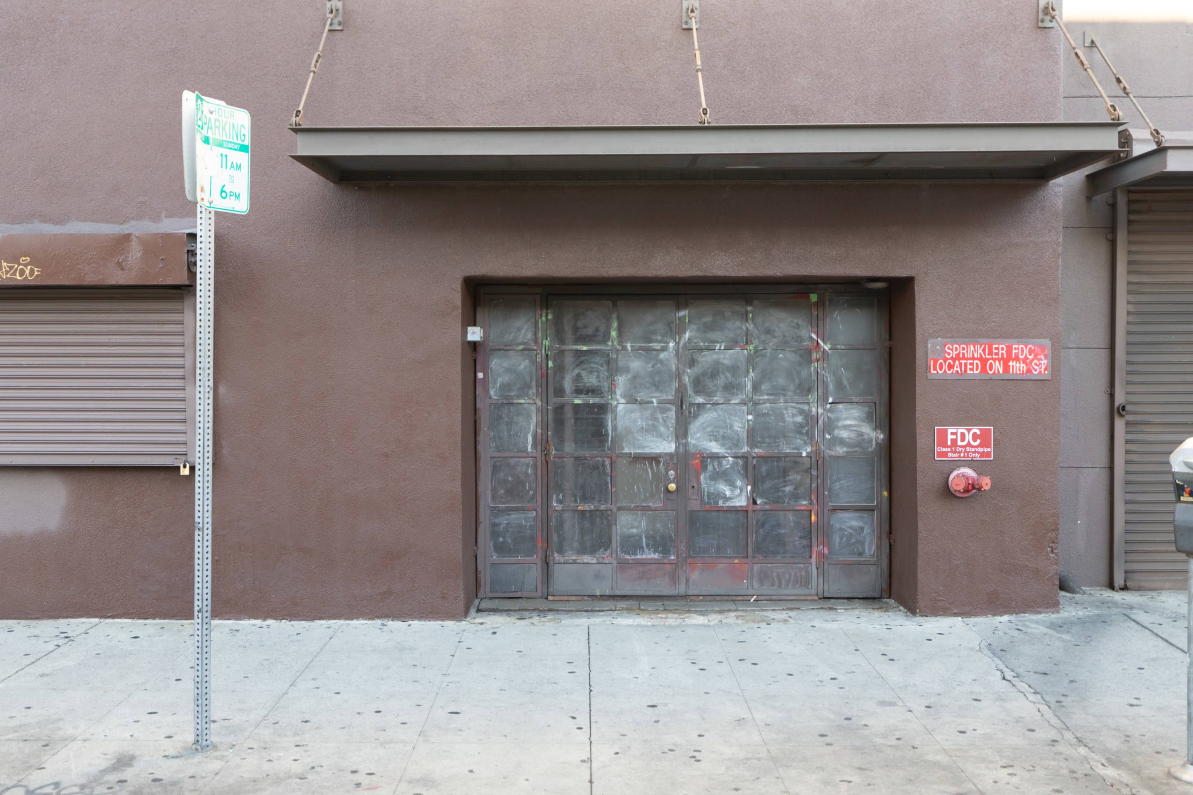 The image shows a brown wall with a large, dirty glass door and a red sign indicating the location of a sprinkler, alongside a parking restriction sign.