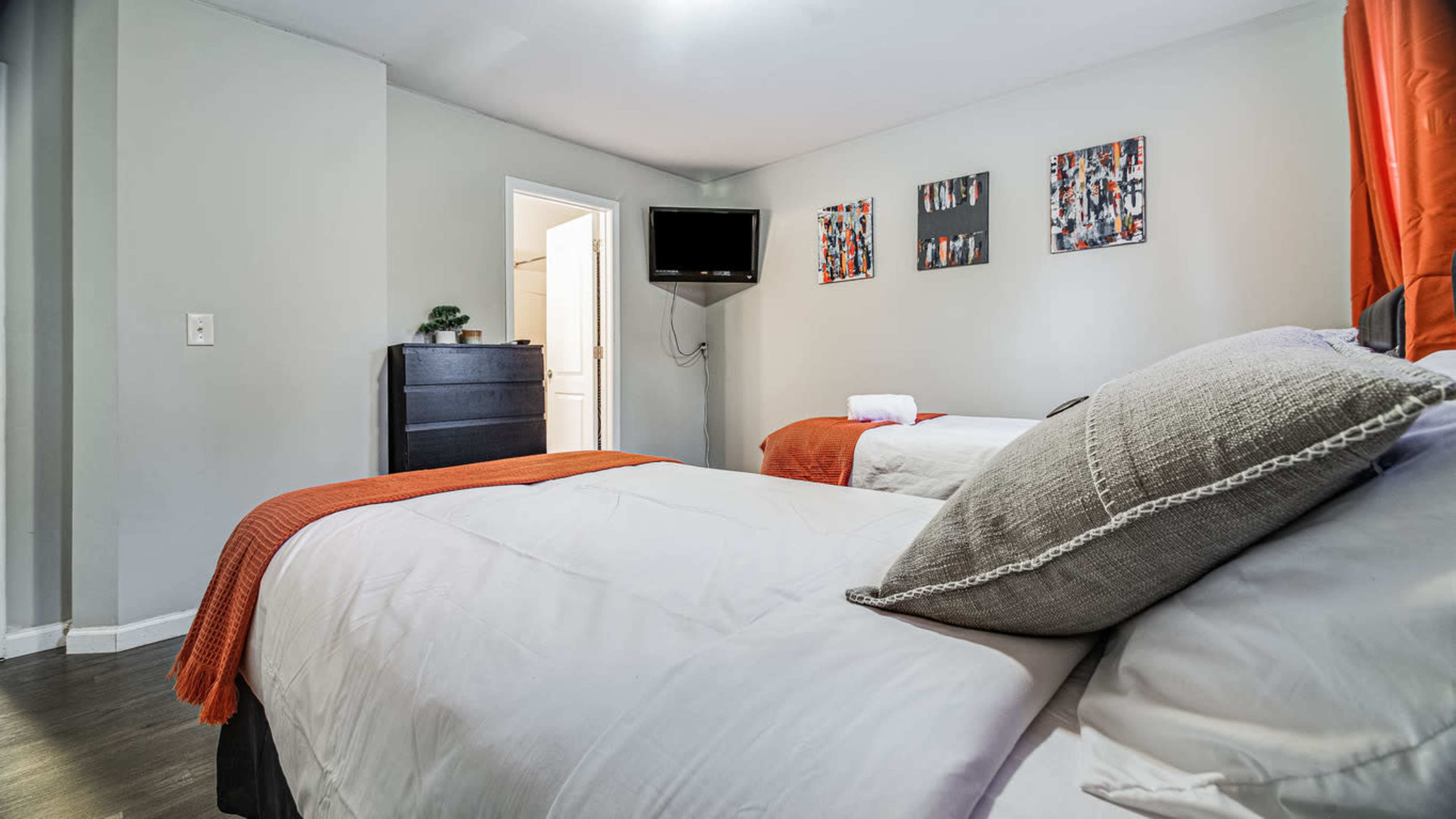 A bedroom with two beds, a television mounted on the wall, and artwork hanging above the beds.