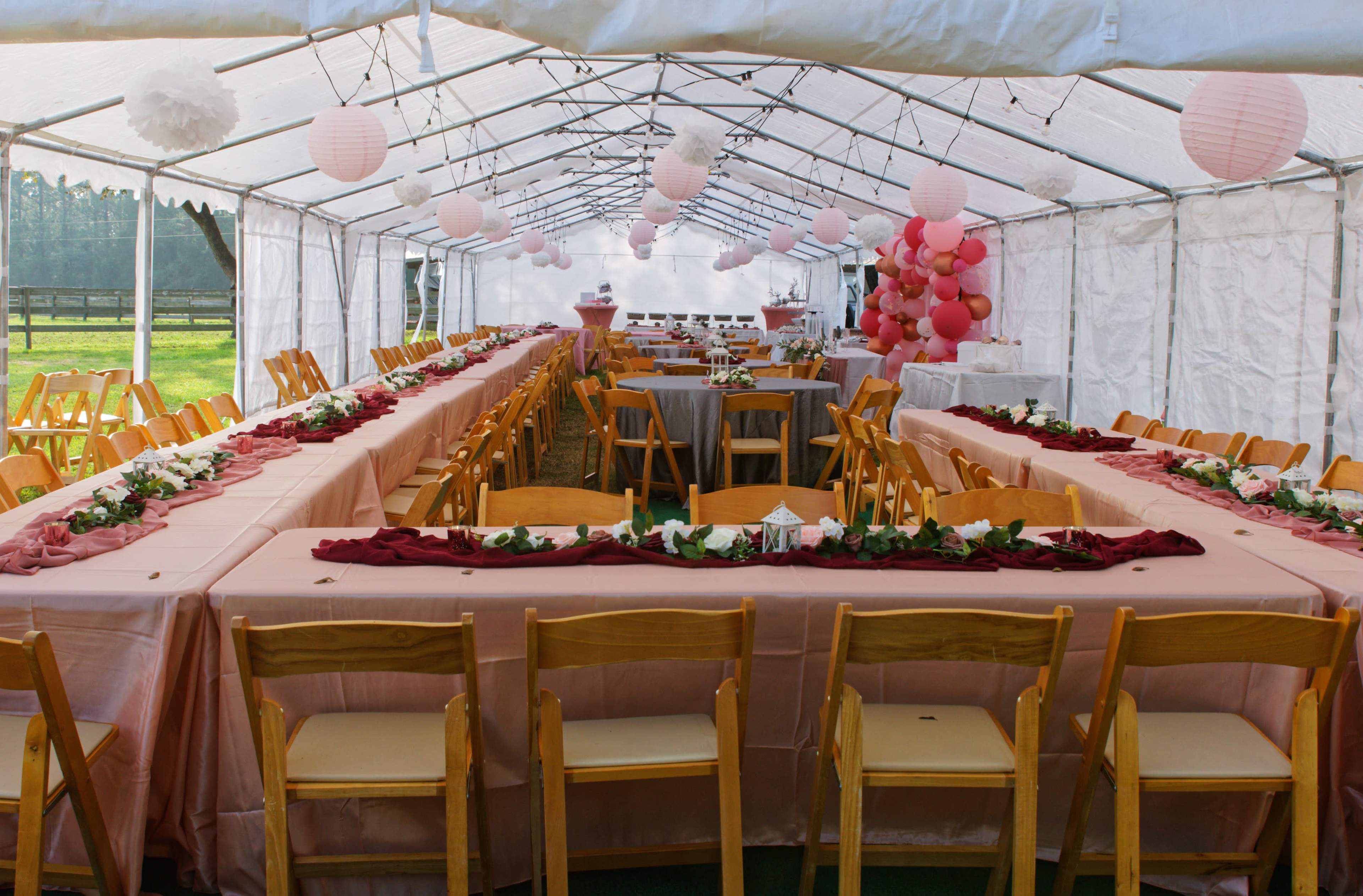A tented event space features long tables adorned with pink tablecloths and floral centerpieces, arranged to accommodate guests.