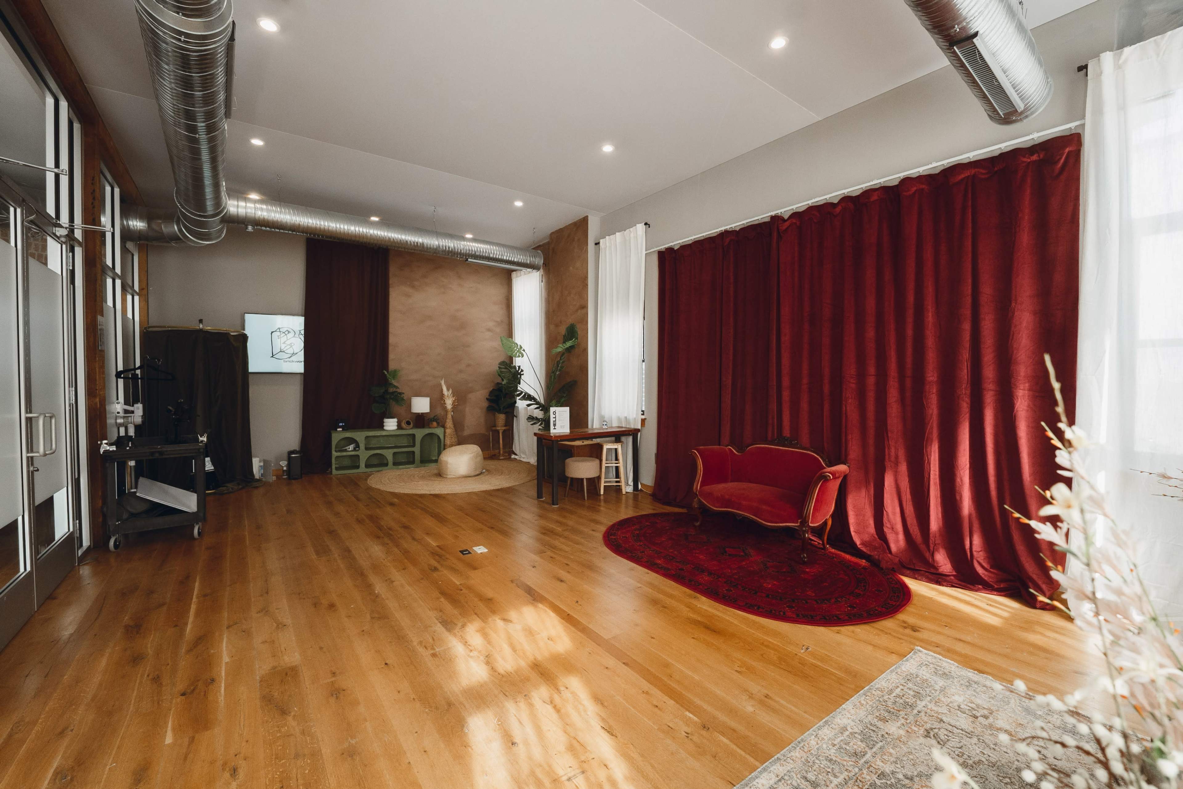 The image shows an interior room with wooden flooring, a red curtain along one wall, a green cabinet, a red rug, a small table, and a vintage-style sofa.