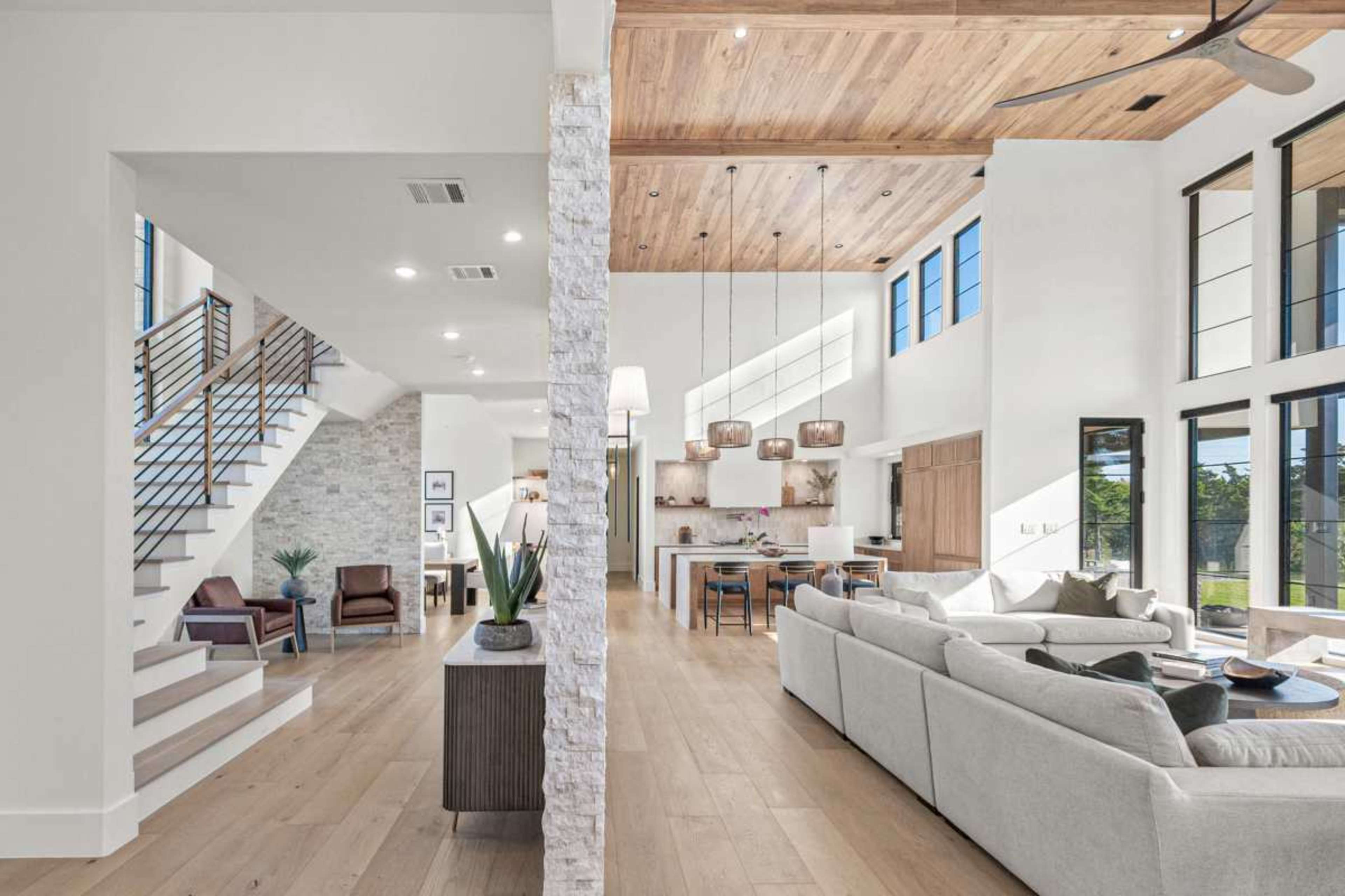 A modern open-concept living space features a spacious seating area, large windows, and a staircase leading to an upper level.