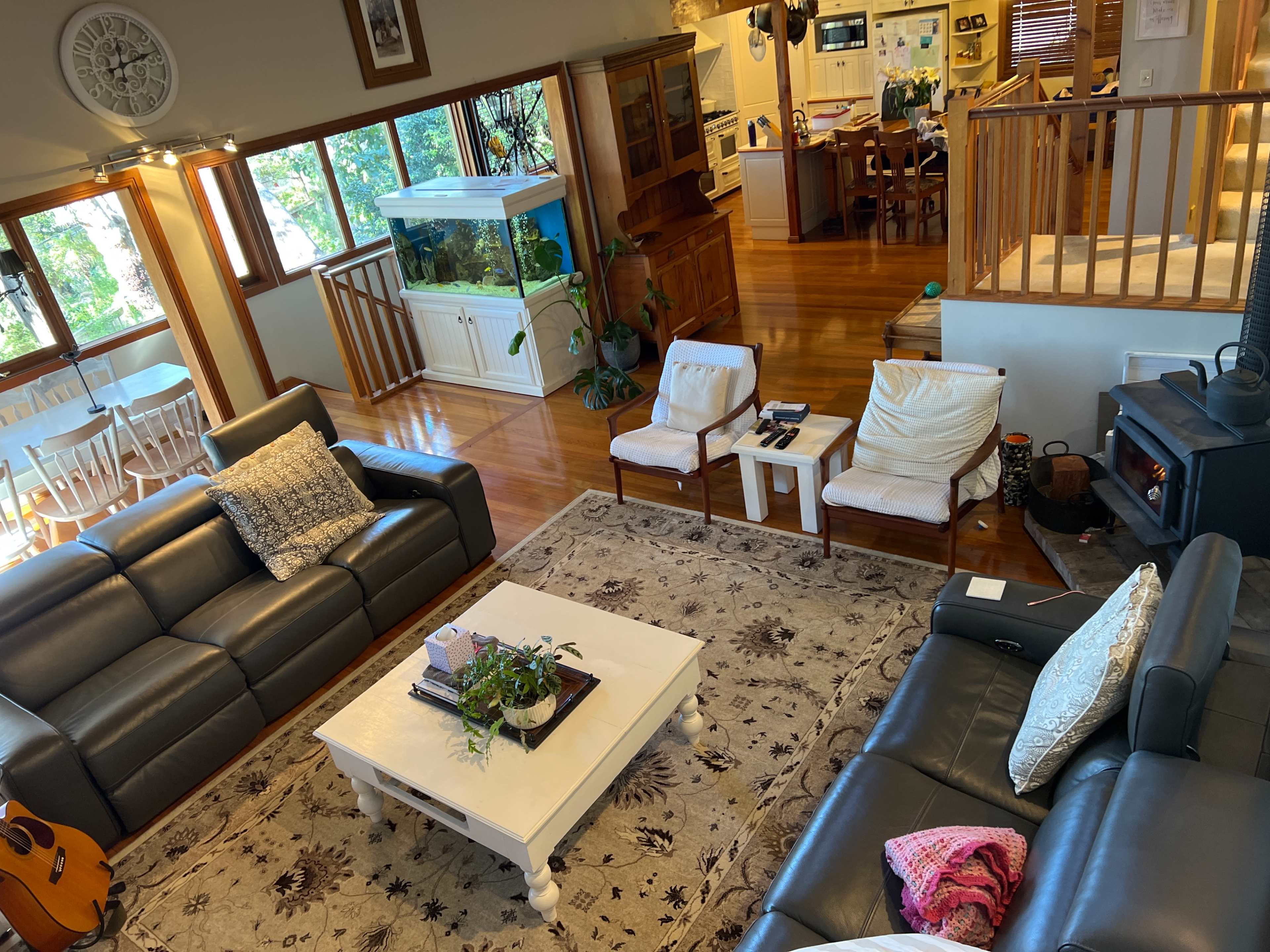 A living room with two dark sofas, a coffee table with a plant, a beige rug, and a dining area visible in the background.