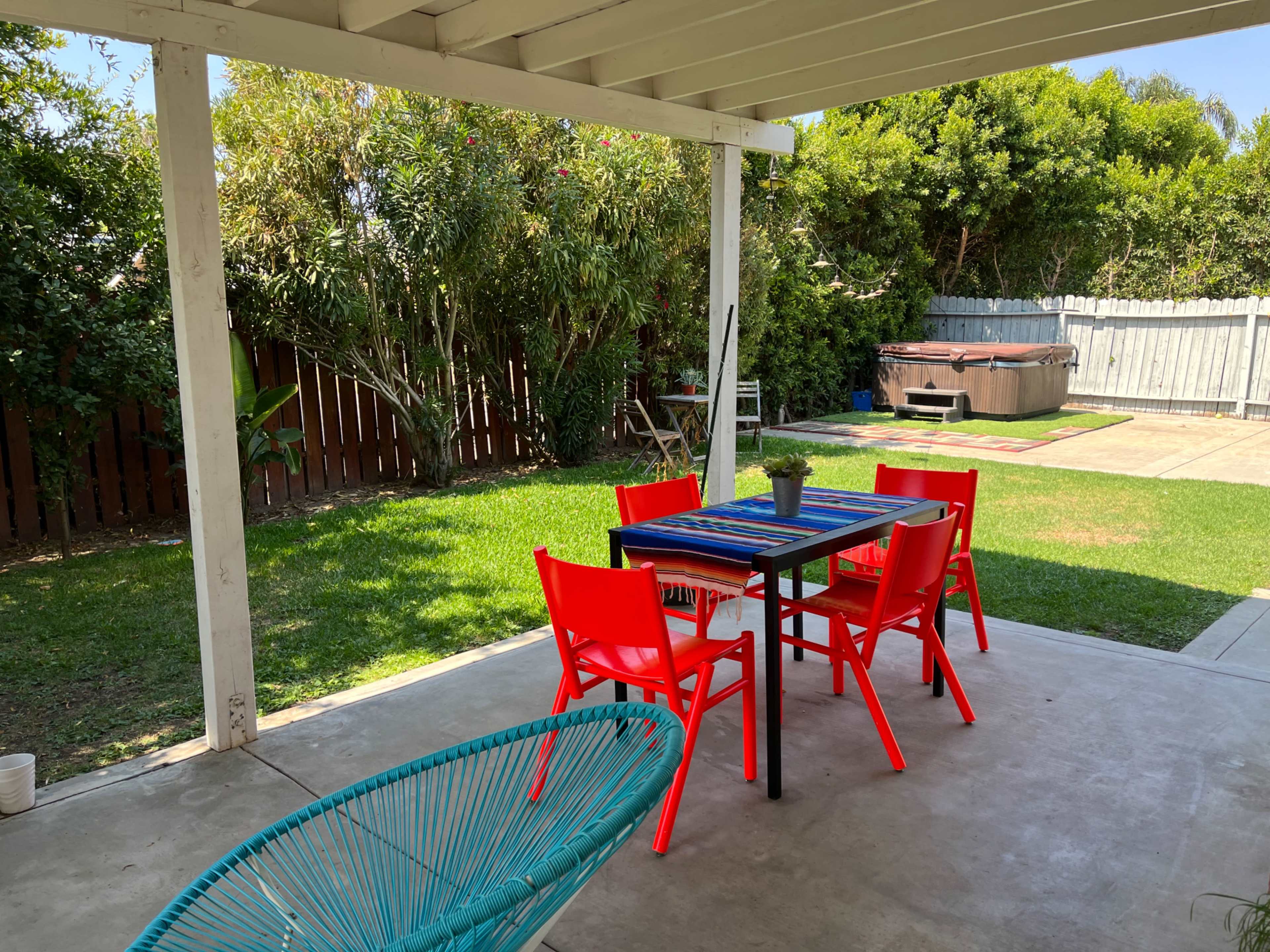 A patio area features a table with colorful chairs, surrounded by a grassy yard and a hot tub in the background.