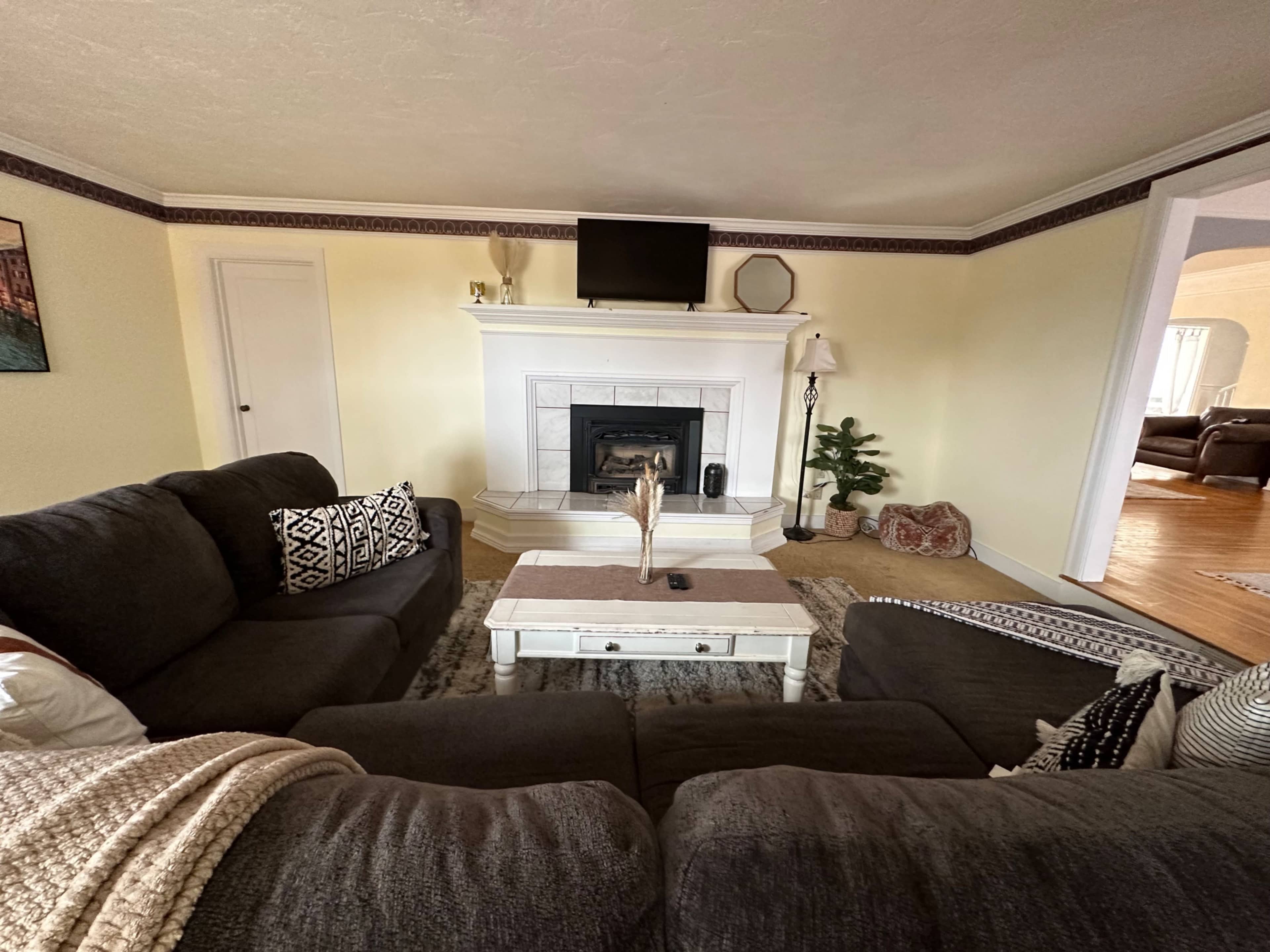 A cozy living room with a fireplace, a television mounted above it, and a sectional sofa arranged around a coffee table.