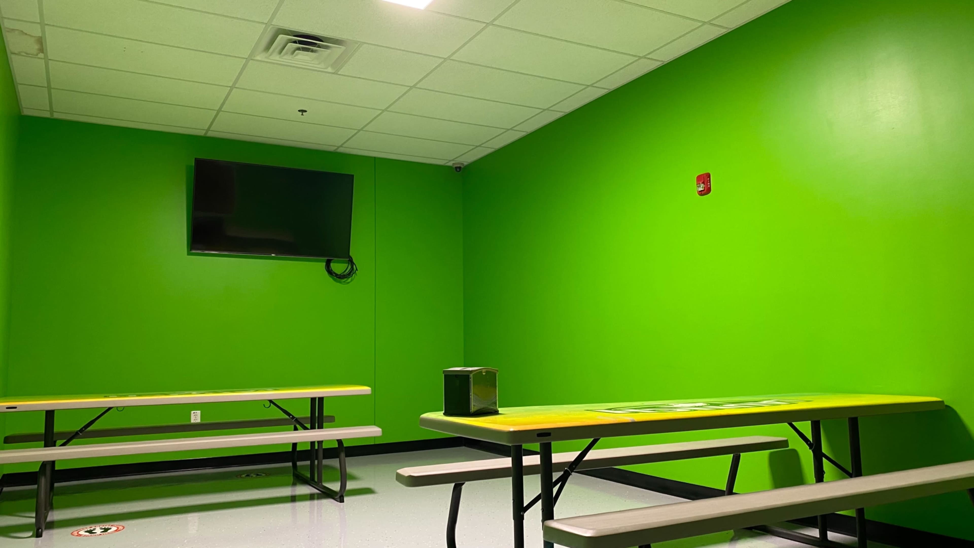 A brightly colored green room with two yellow-topped tables and a wall-mounted television.
