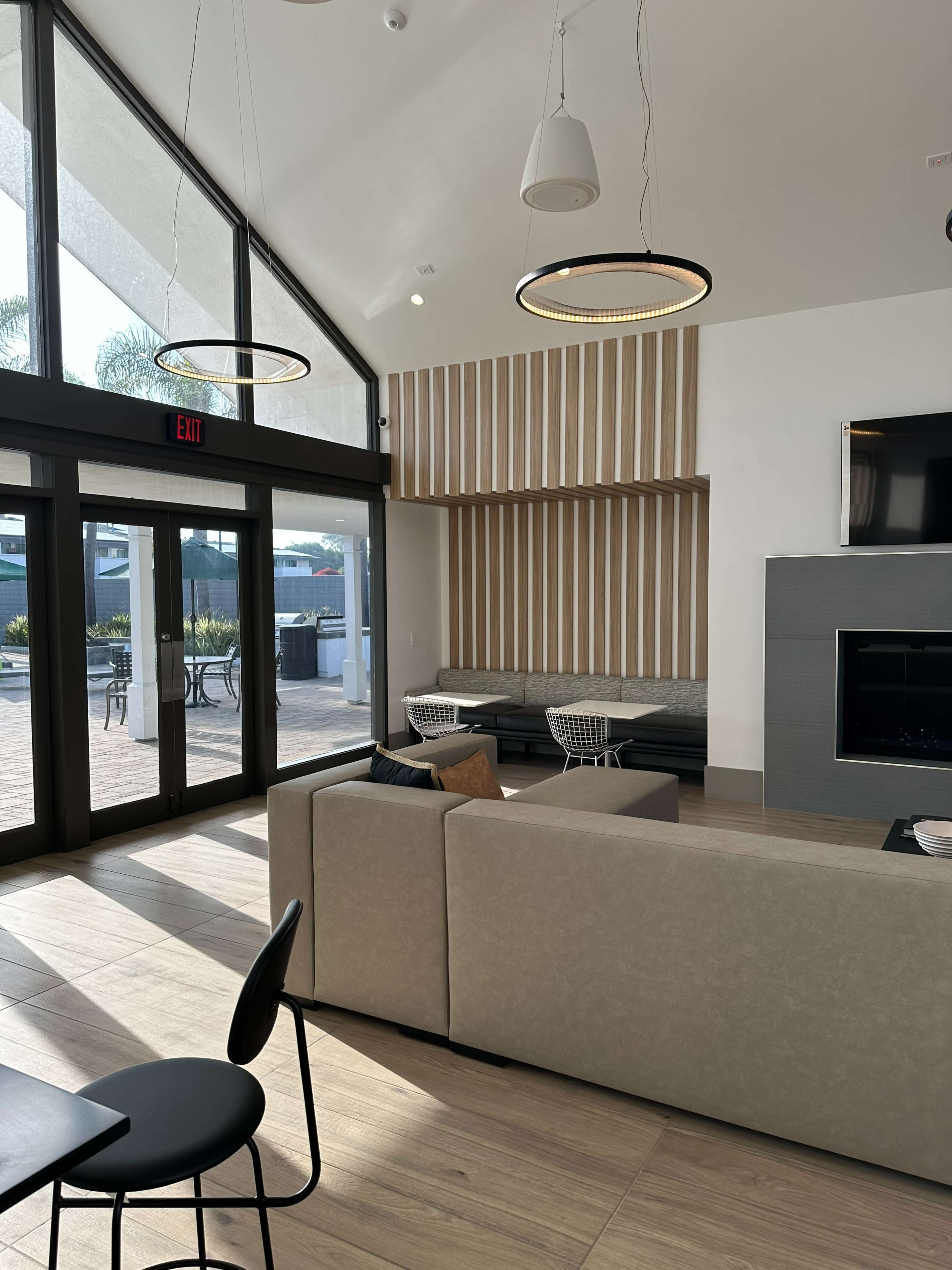 A modern lounge area with large windows, a wall adorned with wooden panels, a sectional sofa, and a fireplace.