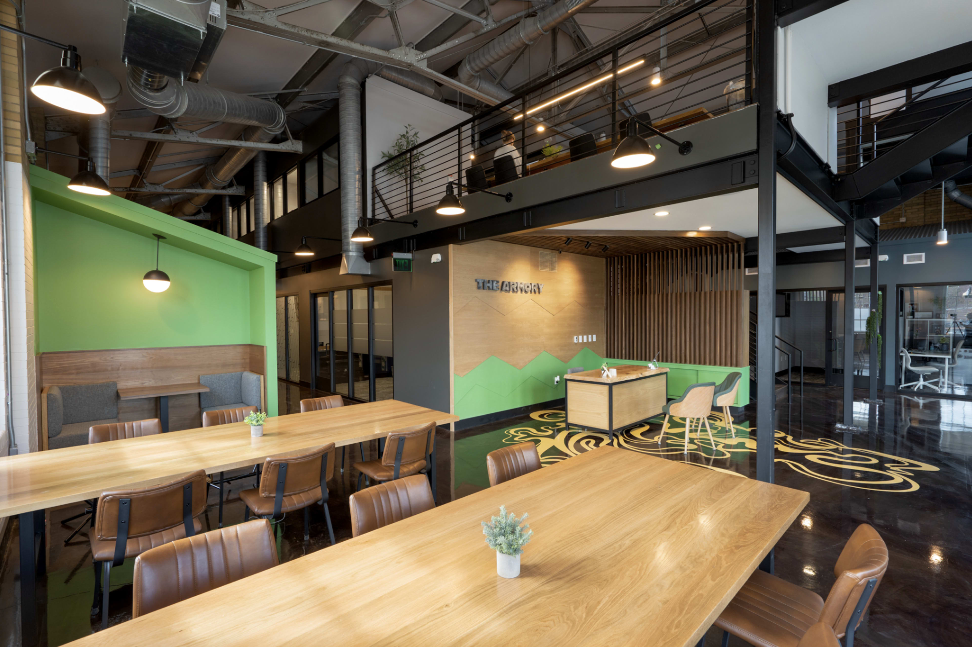 The image shows a modern office space with green and wooden accents, featuring a large wooden table, comfortable chairs, and a reception area with a desk and decorative wall.