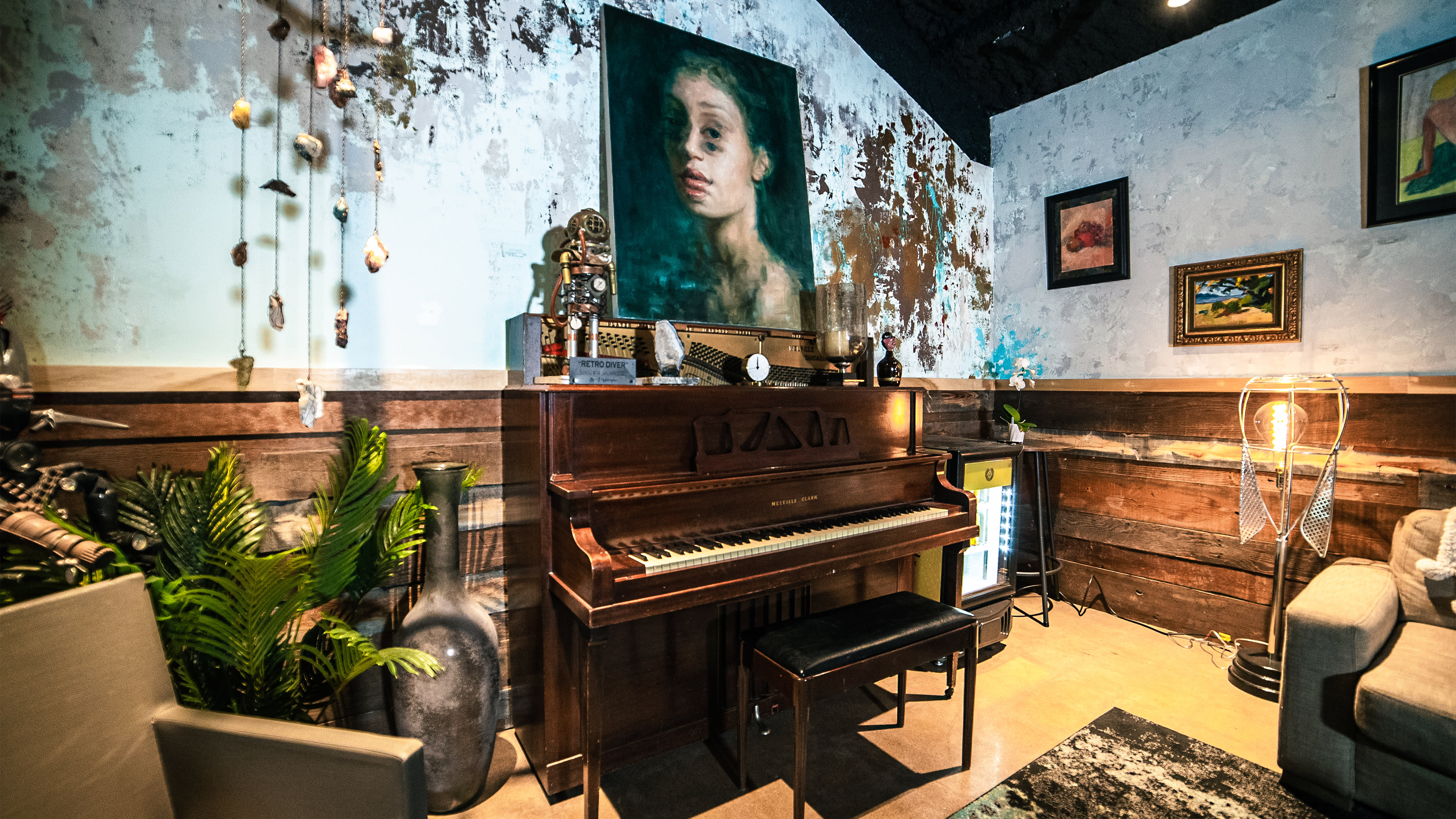 A vintage piano situated in a room with an eclectic decor, including a large painting of a girl on the wall and various artistic objects.
