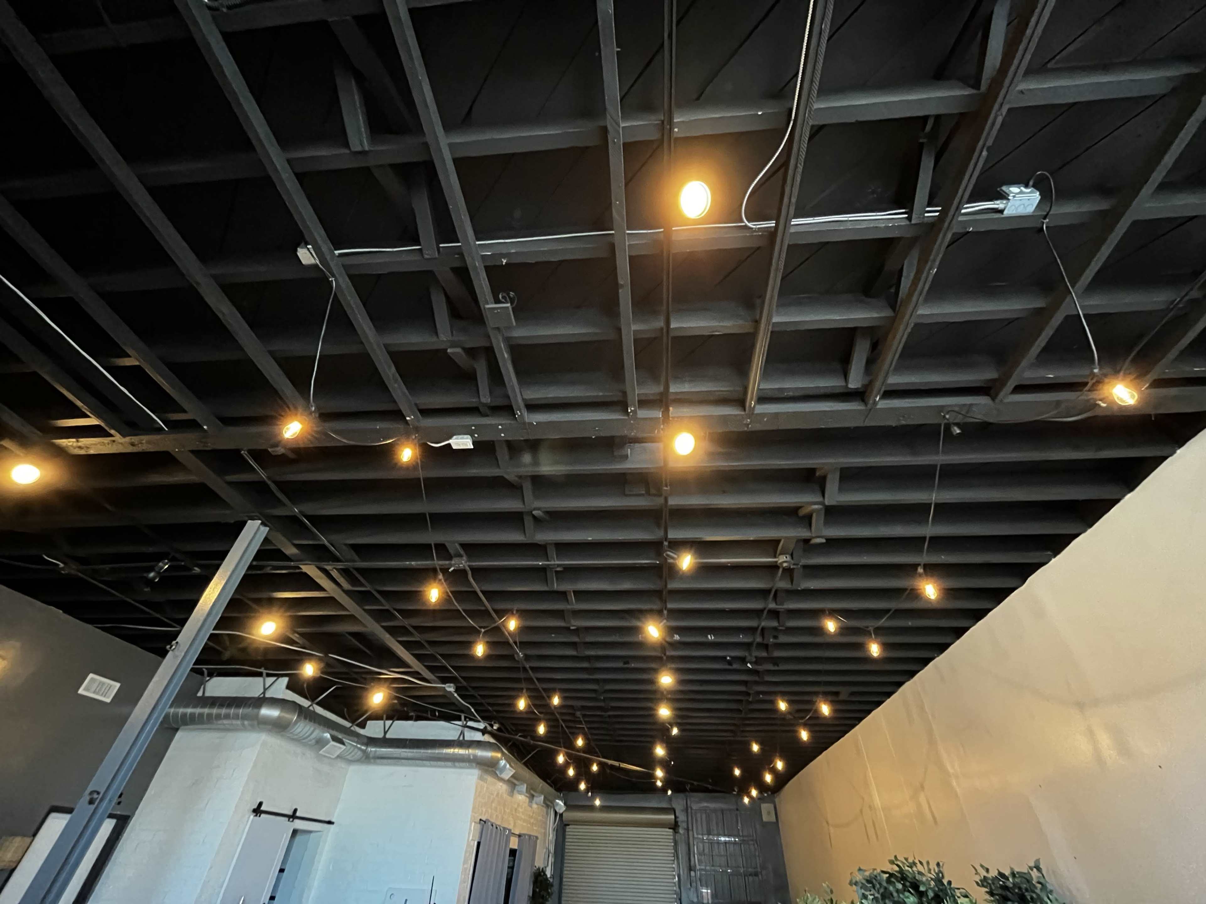 A ceiling with exposed beams and hanging light bulbs, providing soft illumination in a spacious room.