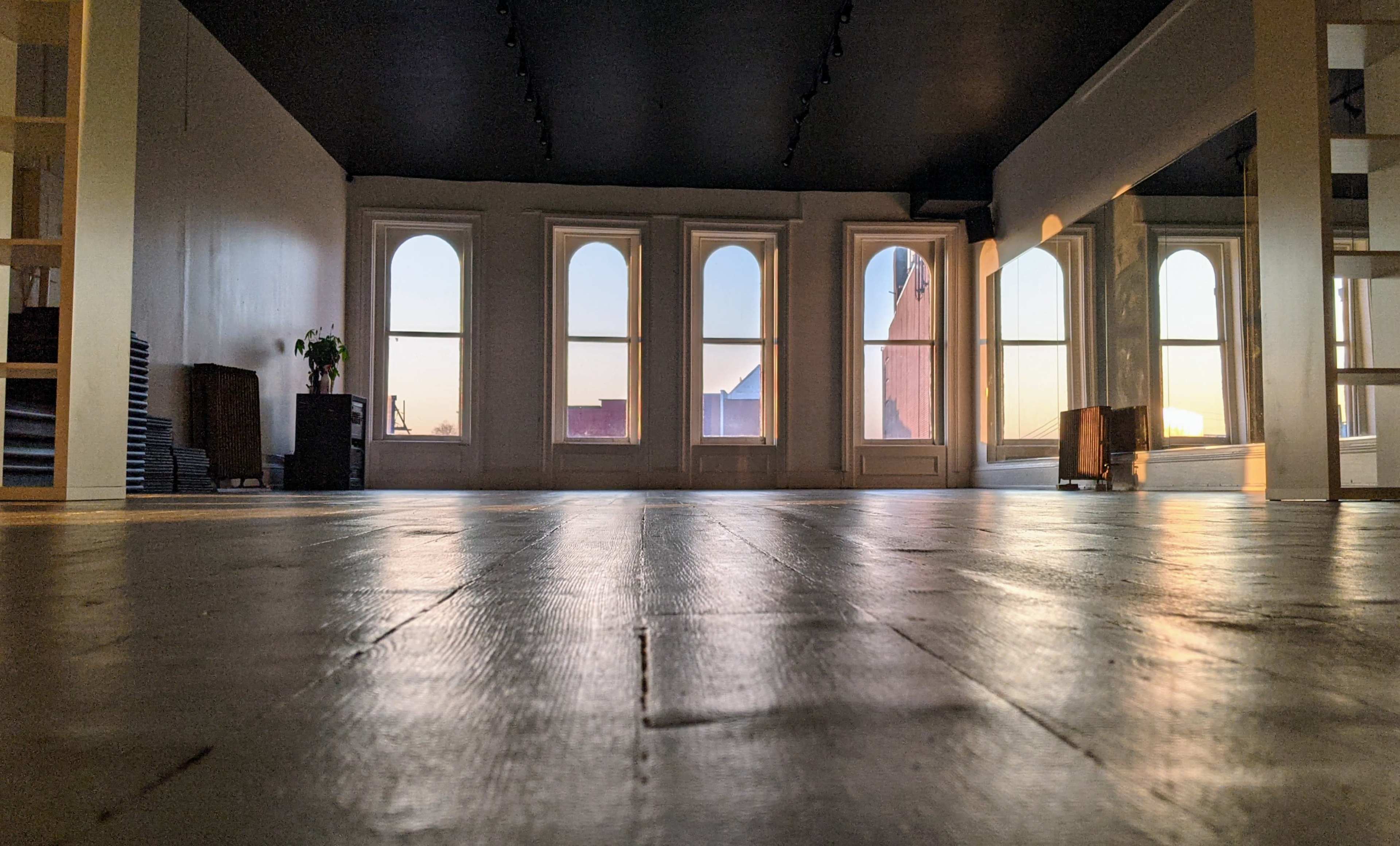 The image shows a spacious room with large arched windows reflecting the warm light from a setting sun.