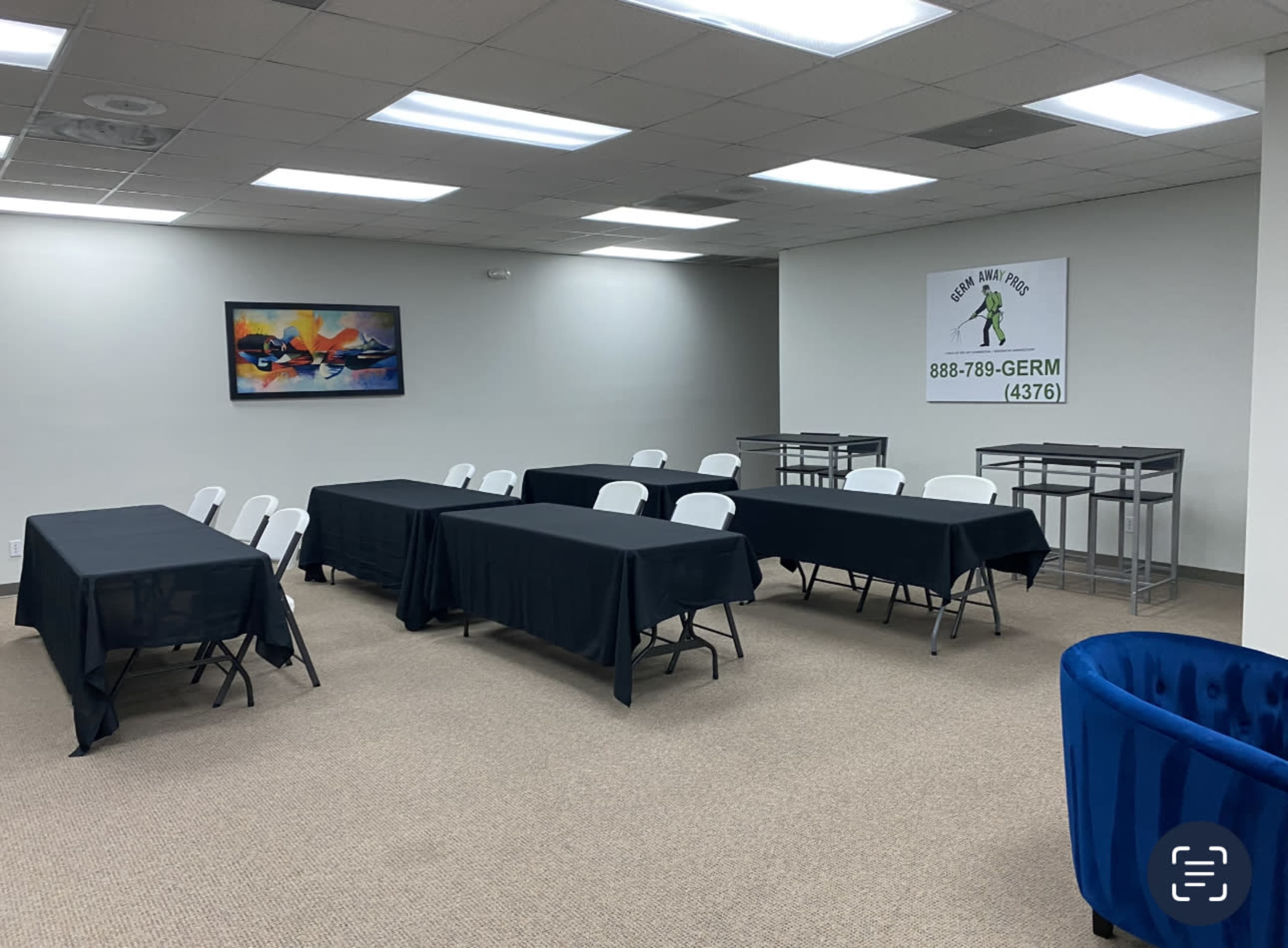 A room set up with several black tables and chairs arranged in rows, along with tall tables against the wall, and a sign displaying a phone number.
