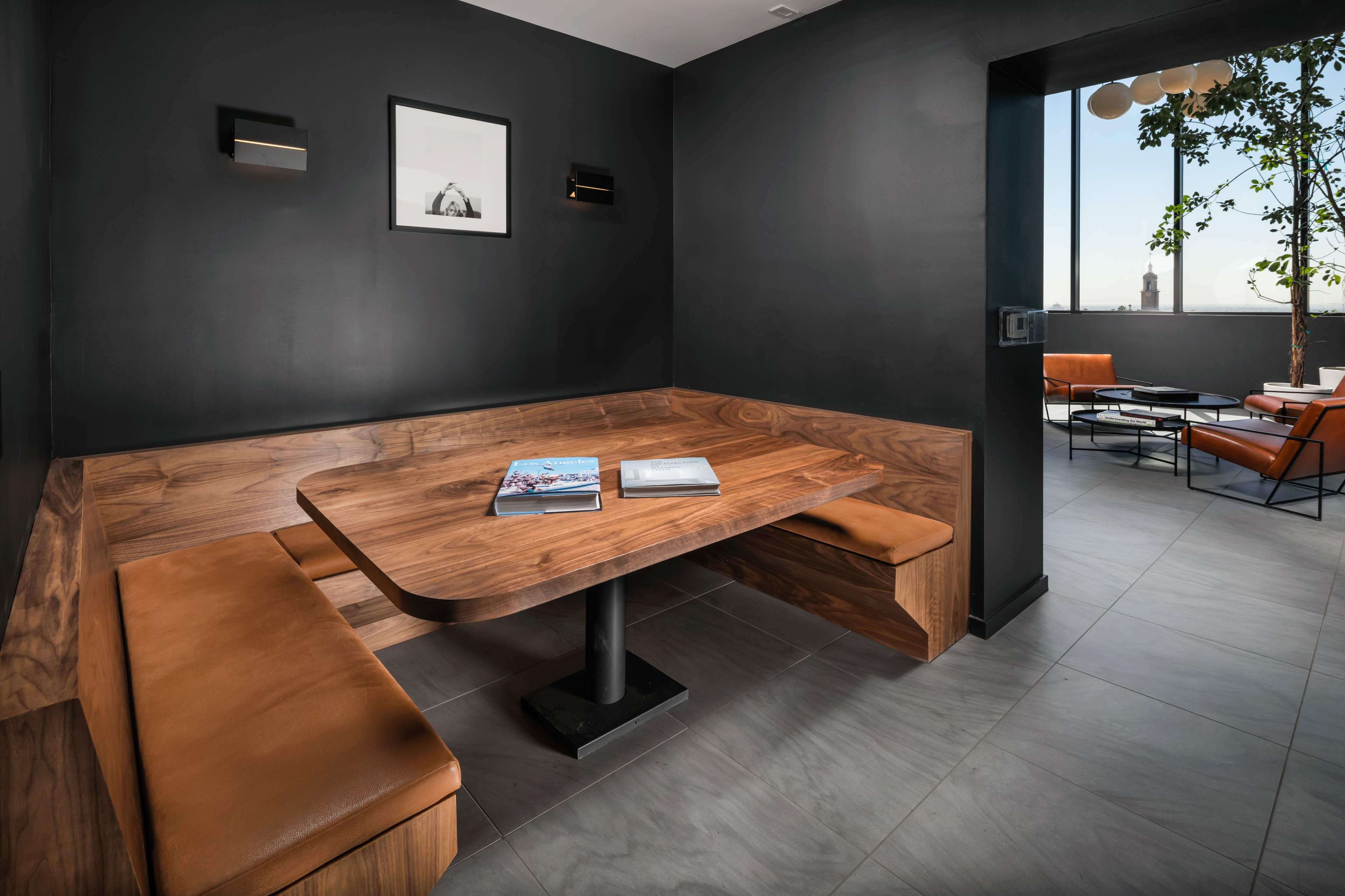 A modern interior space featuring a wooden dining table with built-in seating, complemented by a view of a rooftop terrace through an open doorway.