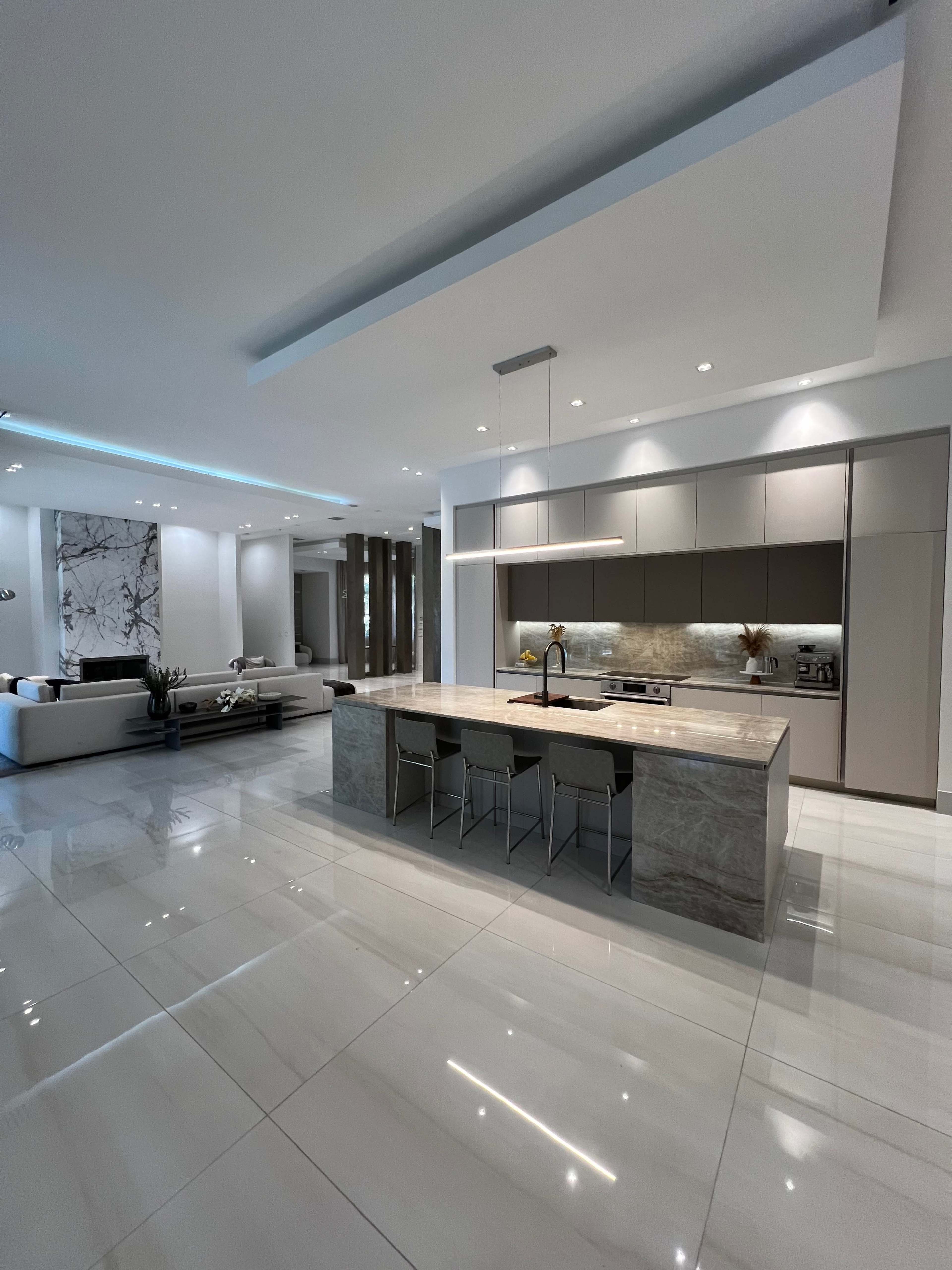 A modern kitchen with a large island, sleek cabinetry, and polished tile flooring in an open-concept living space.