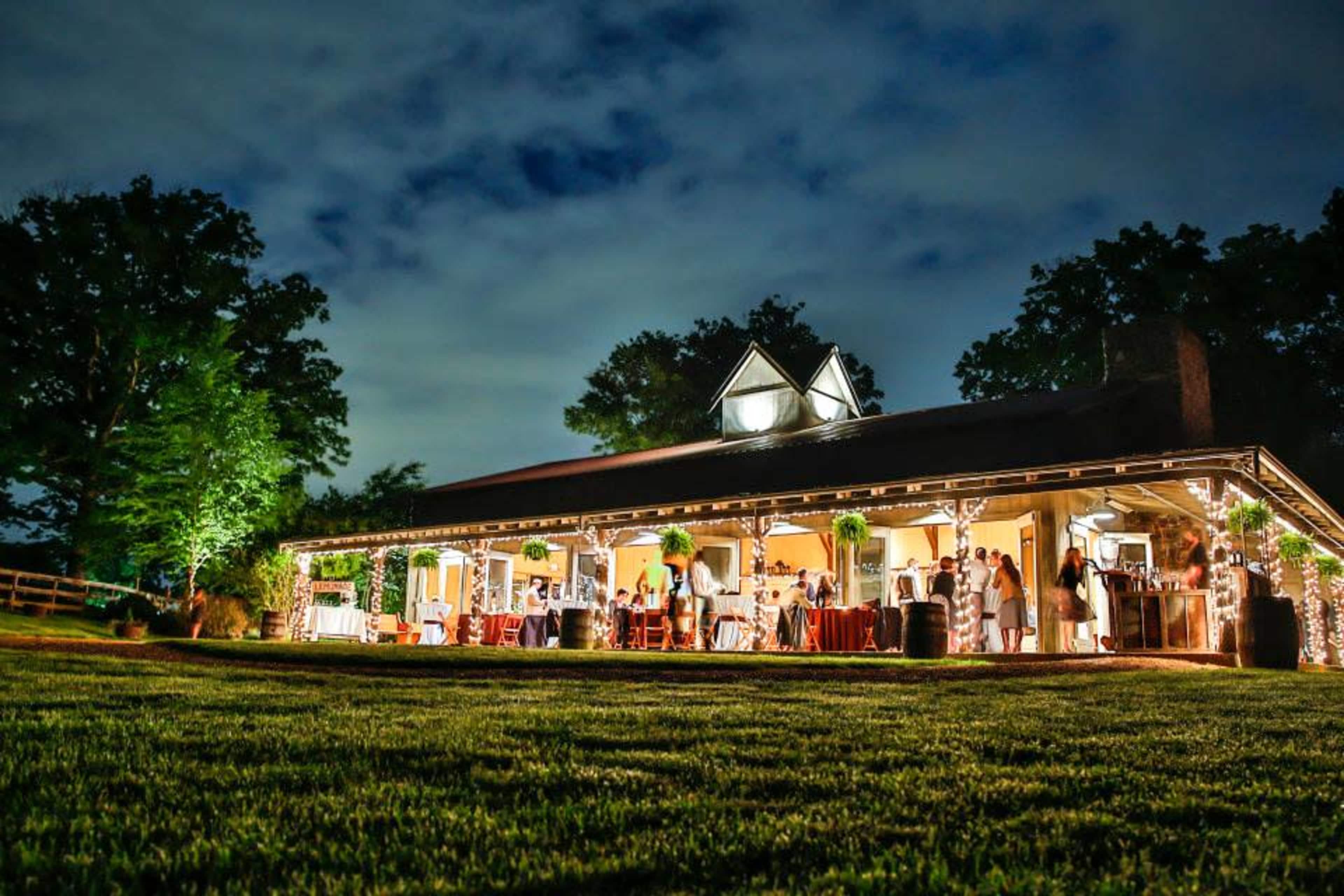 A large, well-lit building with a covered porch hosted a gathering of people in a grassy area under a cloudy sky.